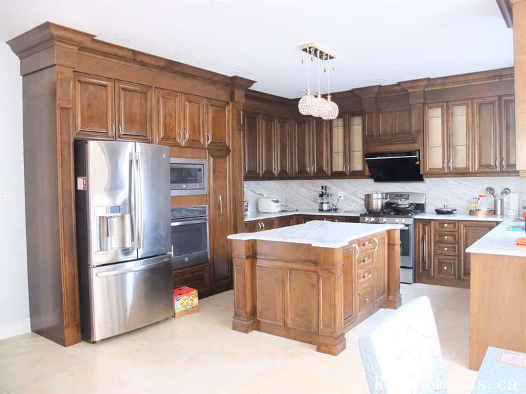 This Richmond Hill kitchen renovation features custom solid wood cabinetry, a large center island with marble countertop, and stainless steel appliances. The elegant traditional kitchen design provides ample storage, improved functionality, and a warm, luxurious atmosphere for daily family living.
