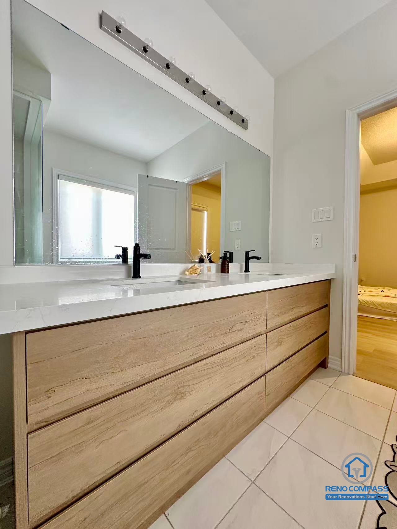 This Stouffville bathroom renovation features a modern double vanity with custom wood cabinetry, a quartz countertop, and matte black fixtures. The oversized mirror and integrated lighting enhance brightness and functionality, creating a clean and comfortable daily-use bathroom. Completed by a trusted Toronto renovation company, Reno Compass Inc., this project highlights refined detailing and practical bathroom design.