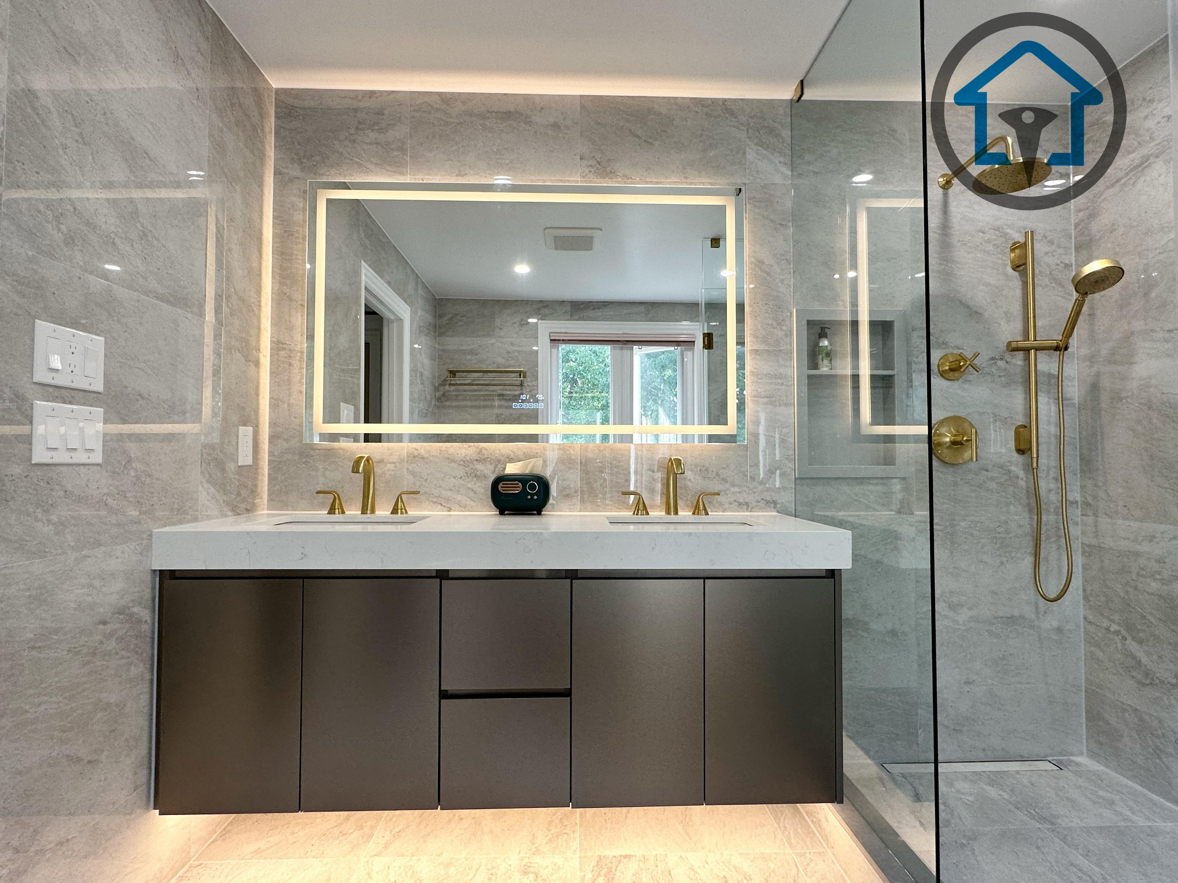 Front view of a modern bathroom completed as part of a North York interior renovation, featuring a custom double-sink vanity, seamless quartz countertop, integrated LED backlit mirror, and brushed gold fixtures. Large-format marble-look wall tiles and a frameless glass shower create a clean, upscale finish, delivered by a professional Toronto renovation company focused on precision and long-term durability.