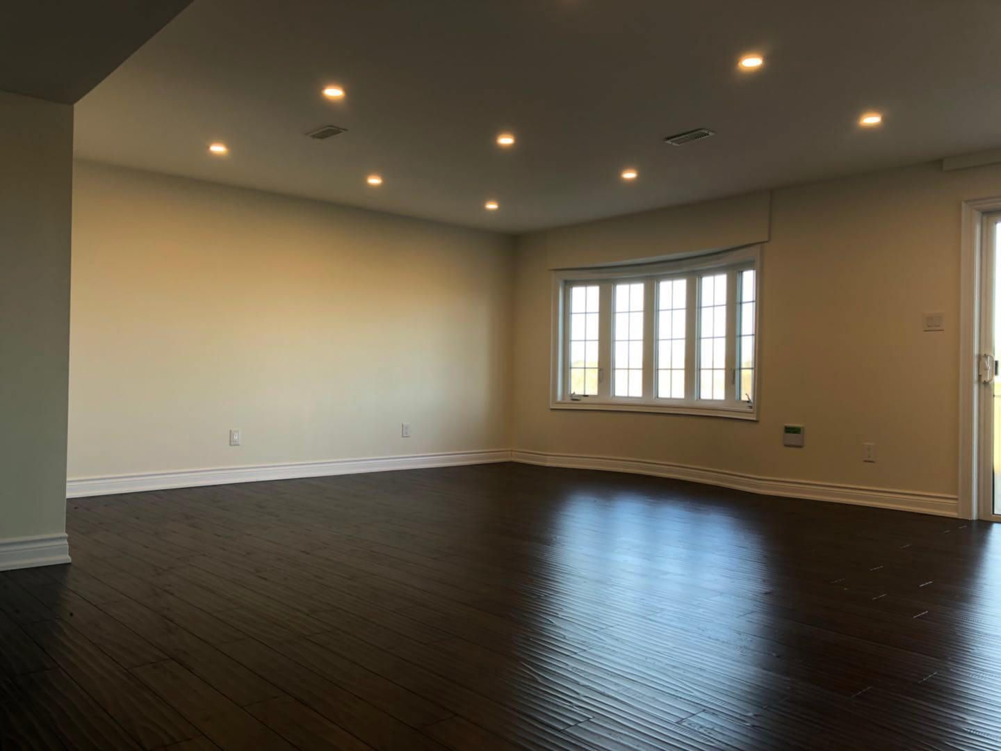 Spacious open-concept living area completed as part of a Toronto basement renovation project, featuring dark hardwood flooring, recessed pot lighting, smooth ceiling finish, and large window installation to maximize natural light in the lower level.