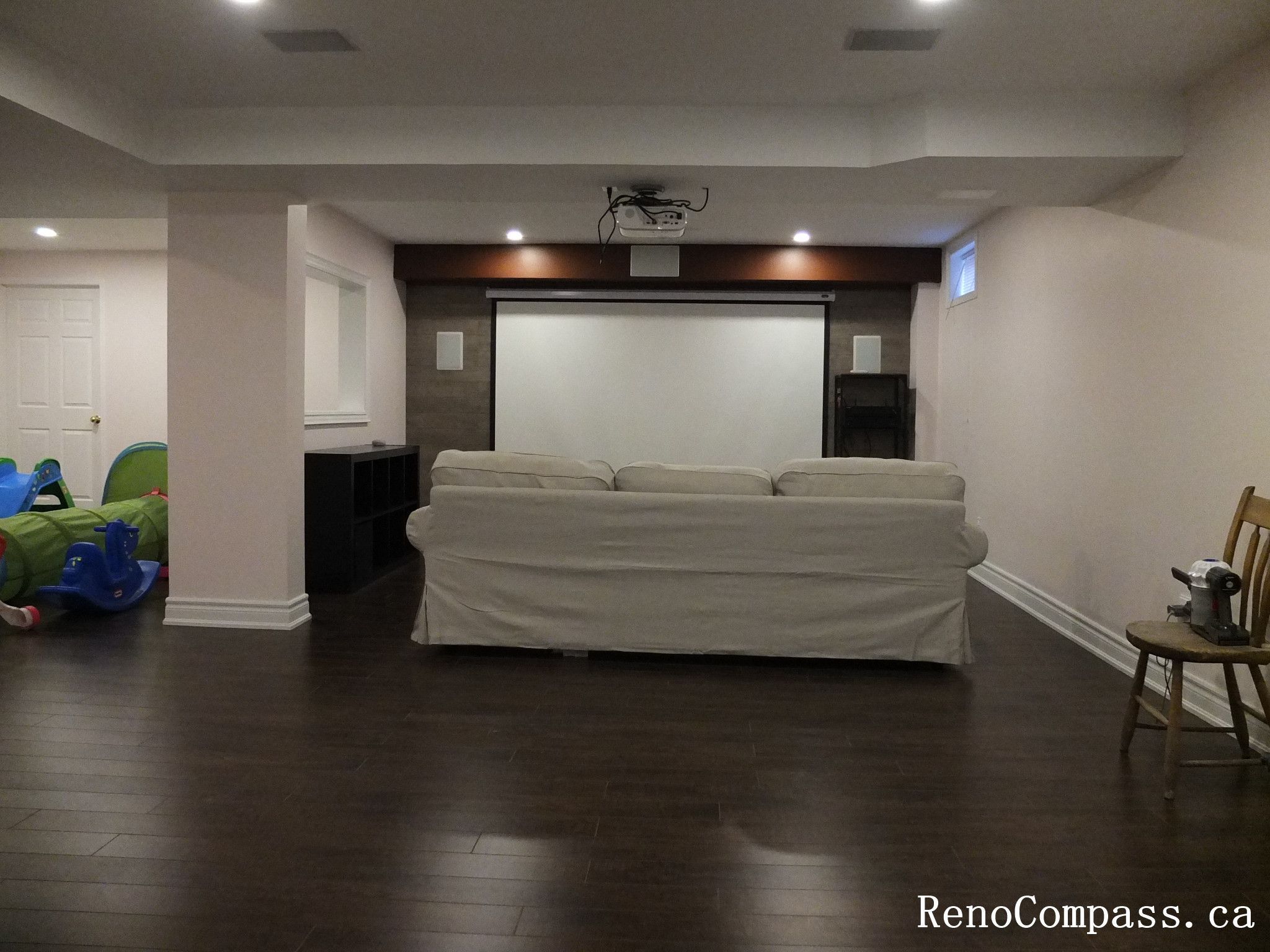 Modern basement interior renovation in Newmarket featuring a custom home theater setup, dark hardwood flooring, built-in shelving, recessed lighting, and a projector screen. Professionally completed by a Toronto Renovation Company to create a functional entertainment space for the whole family.
