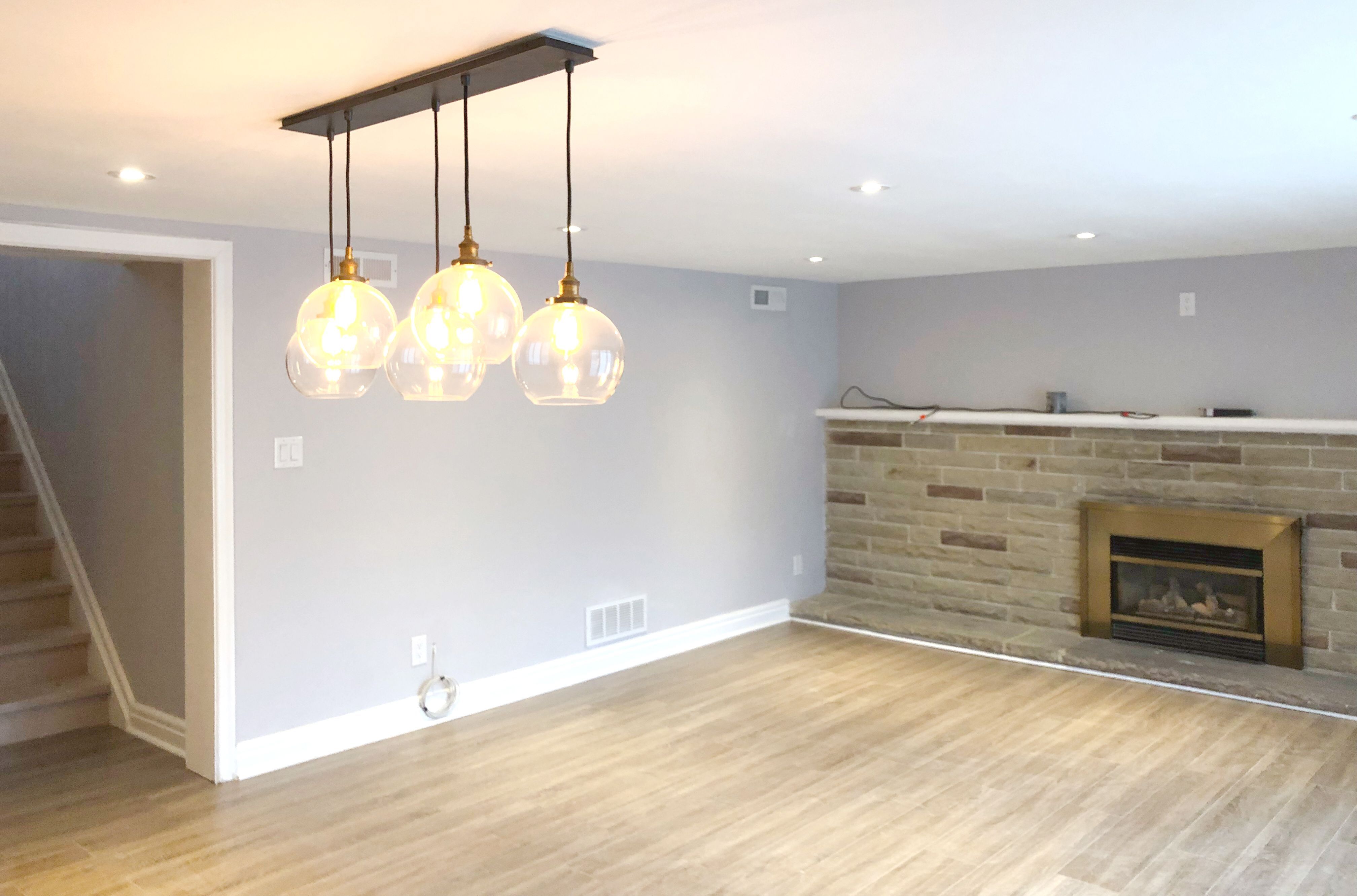 This Etobicoke interior renovation features a refreshed living space with upgraded flooring, modern pendant lighting, and a feature fireplace wall that adds warmth and visual focus. Neutral wall tones and recessed lighting create a bright and comfortable atmosphere, while the open layout improves flow between living and dining areas. Completed by Reno Compass Inc., this renovation enhances everyday comfort with a clean, modern design and practical layout improvements suitable for contemporary family living.