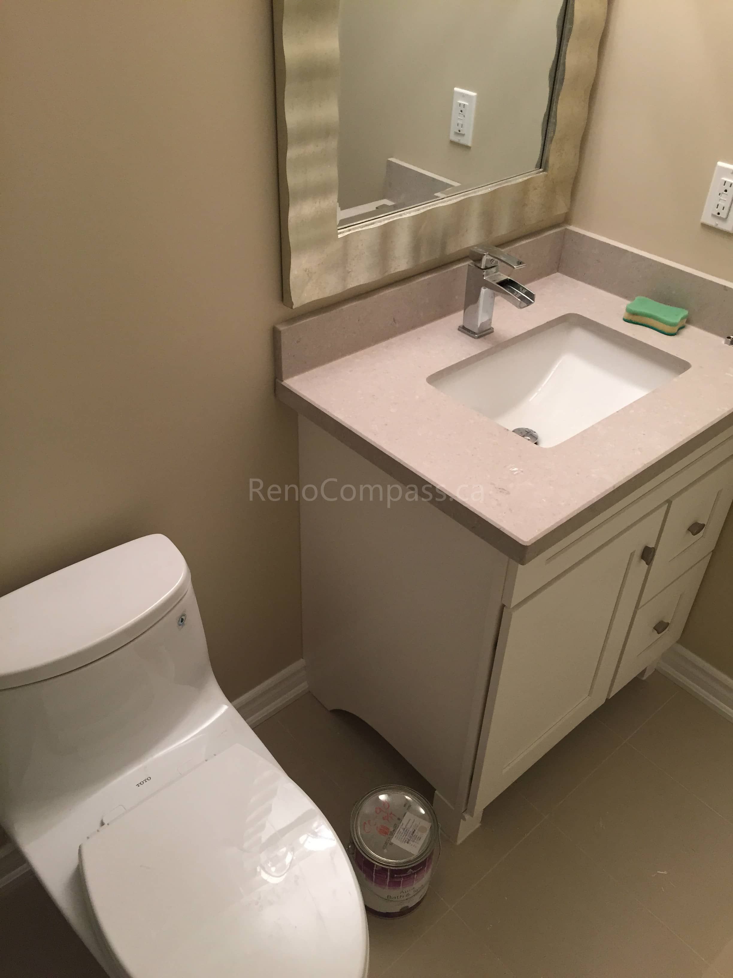 This Toronto bathroom renovation features a newly installed vanity with a quartz countertop, modern faucet, and framed mirror, paired with a sleek contemporary toilet. The neutral wall tones and clean layout create a bright and functional powder room space. Designed for both style and practicality, the renovation enhances comfort and everyday usability. Completed by Reno Compass Inc., this project highlights professional bathroom renovation and interior finishing services in Toronto.