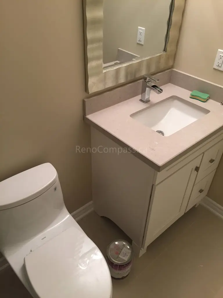 This Toronto bathroom renovation features a newly installed vanity with a quartz countertop, modern faucet, and framed mirror, paired with a sleek contemporary toilet. The neutral wall tones and clean layout create a bright and functional powder room space. Designed for both style and practicality, the renovation enhances comfort and everyday usability. Completed by Reno Compass Inc., this project highlights professional bathroom renovation and interior finishing services in Toronto.