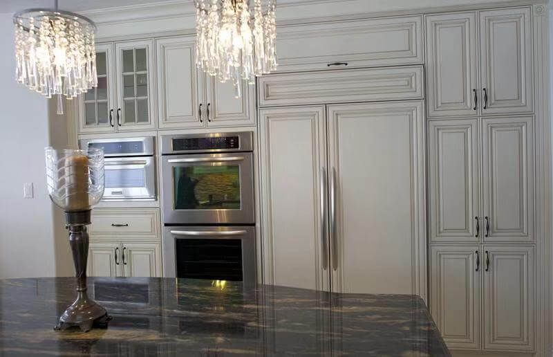 This European-style kitchen renovation showcases elegant custom white cabinetry with detailed panel molding and classic hardware, creating a refined and timeless aesthetic. The kitchen features a fully integrated built-in refrigerator and double wall ovens, maximizing functionality while maintaining a seamless design.

The large central island is finished with a dark natural stone countertop, adding contrast and sophistication to the space. Crystal chandeliers enhance the luxurious European atmosphere, combining traditional charm with modern convenience.

This kitchen design is ideal for homeowners seeking a high-end, classic European kitchen upgrade with enhanced storage, premium finishes, and a cohesive layout.