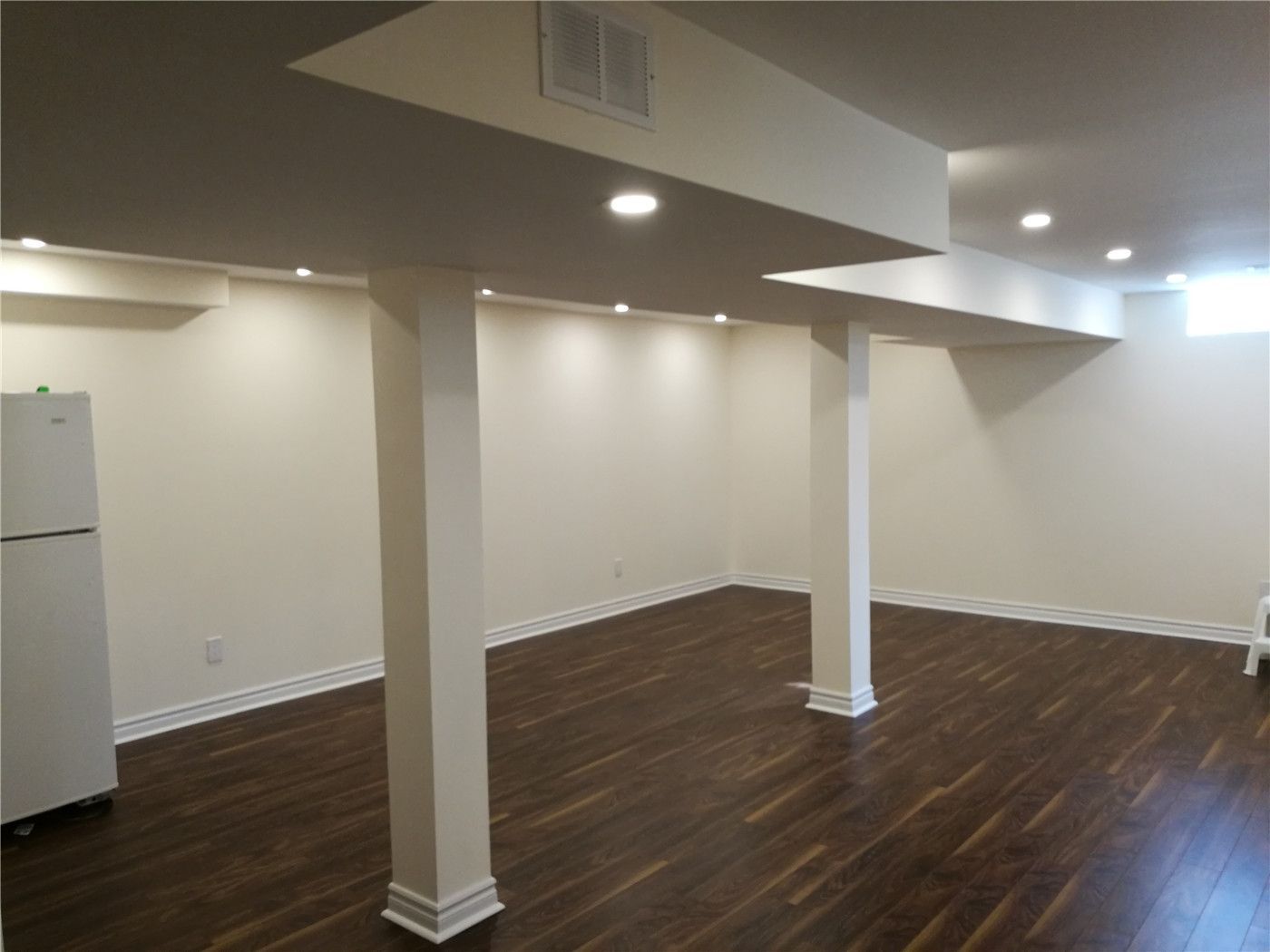 This Aurora basement renovation project features newly installed dark hardwood flooring, a clean drywall ceiling with integrated pot lights, and a bright, open layout that maximizes usable living space. Structural beams and support columns are neatly finished to maintain a modern and uncluttered appearance. The renovated basement is ideal for a family room, home gym, or multi-purpose living area. Completed by a professional Toronto renovation company, this project enhances both comfort and property value for the homeowner in Aurora.
