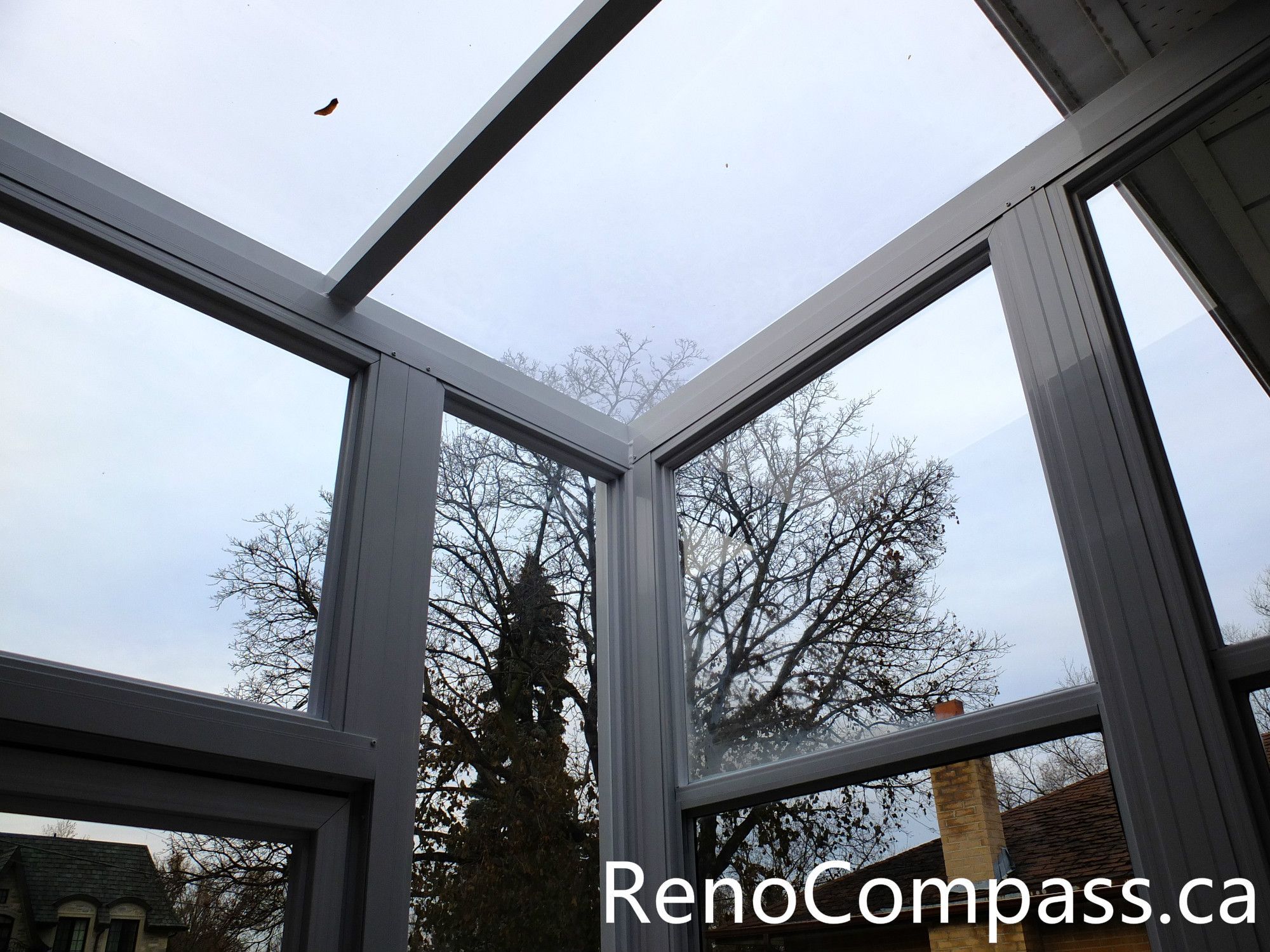 This close-up image highlights the hinge and support mechanism of a custom glass storm door installed at a North York home entrance. The reinforced metal hinge, spring support, and secure frame structure ensure smooth operation and long-term durability while protecting the main entrance from wind, snow, and rain. The white aluminum frame and transparent glass panels create a clean and modern entry vestibule design. Installed by a professional Toronto renovation team, this storm door system improves both functionality and weather protection for the home entrance.
