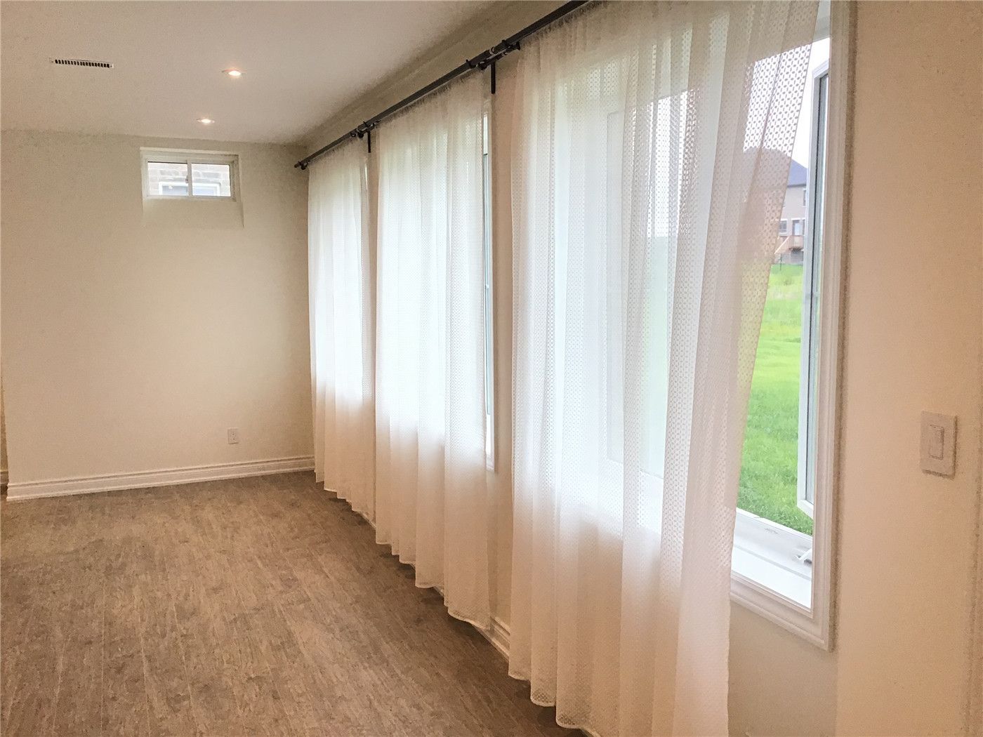 This Aurora interior renovation highlights a bright basement space with large windows, soft sheer curtains, and wood-look vinyl flooring. The design enhances natural light while maintaining privacy, creating a warm and inviting atmosphere suitable for a living area or bedroom.