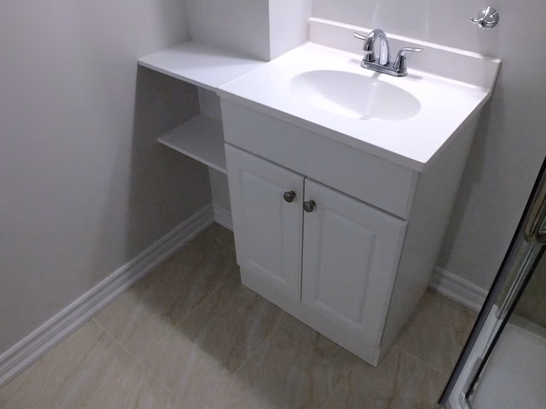This Richmond Hill basement bathroom renovation showcases a clean and functional white vanity with an integrated sink, chrome faucet, and custom side shelving for added storage. The compact design maximizes space efficiency while maintaining a modern and minimal aesthetic. Completed by a professional Toronto renovation company, this basement bathroom upgrade improves daily usability and adds long-term value to the home.