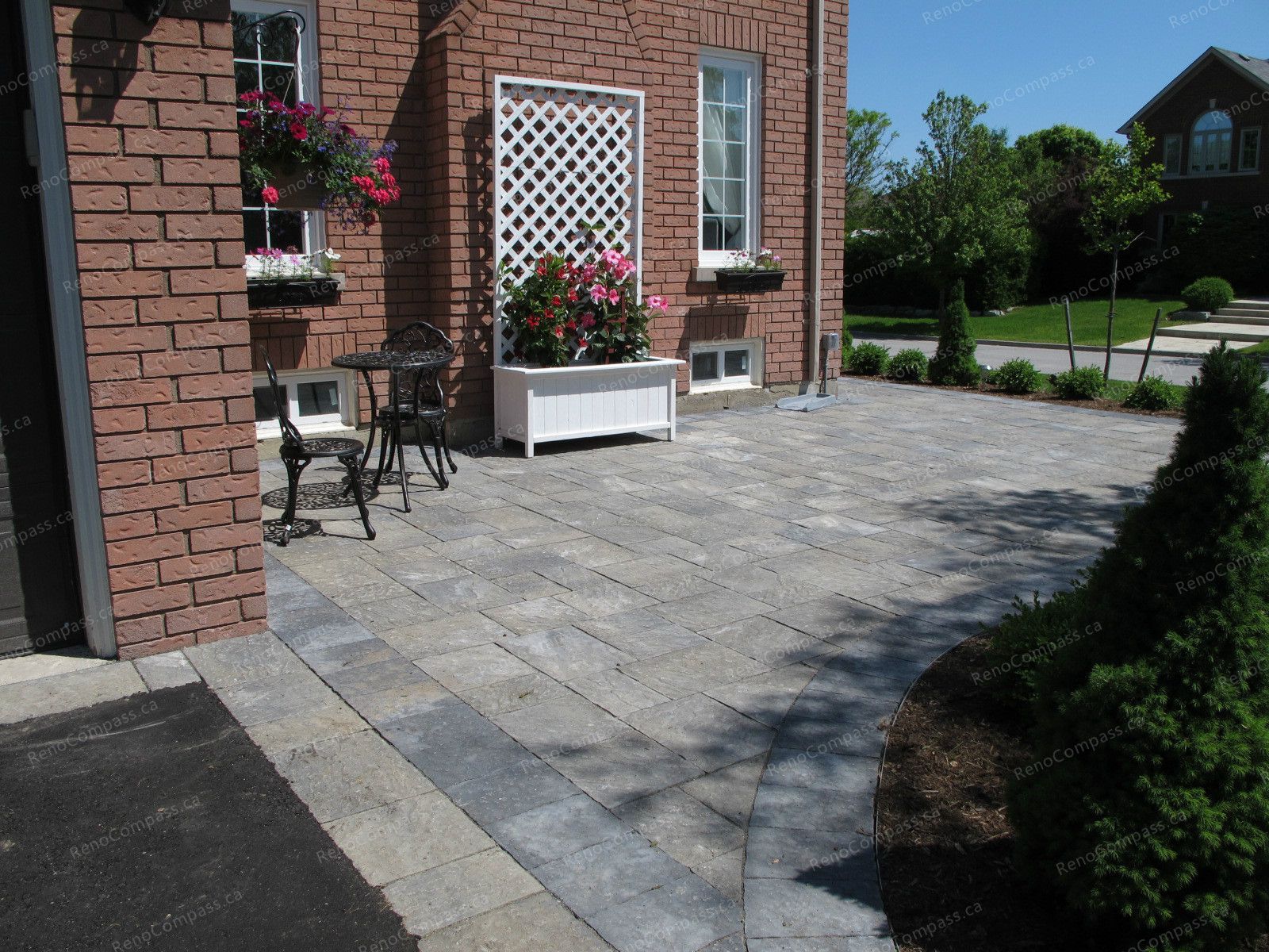 This image highlights a finished outdoor landscaping project in Newmarket, featuring a clean interlock patio design integrated with garden planters and a small seating area. The natural-tone stone pavers create a smooth, durable surface that enhances both functionality and visual continuity with the surrounding garden. Decorative planters, climbing trellis details, and soft greenery add warmth and charm to the space, making it ideal for outdoor relaxation and everyday use. This landscaping project demonstrates thoughtful layout planning, quality craftsmanship, and long-lasting exterior design.