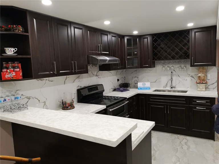 This image showcases a completed kitchen from a Newmarket interior renovation project, featuring dark wood cabinetry, a white quartz countertop, and a matching waterfall island design. The kitchen includes custom storage, integrated appliances, a modern range hood, and recessed pot lighting that enhances brightness and functionality. The clean contrast between dark cabinets and light surfaces creates a timeless and elegant look. Completed by a professional Toronto renovation company, this kitchen renovation improves workflow, storage efficiency, and overall home value.