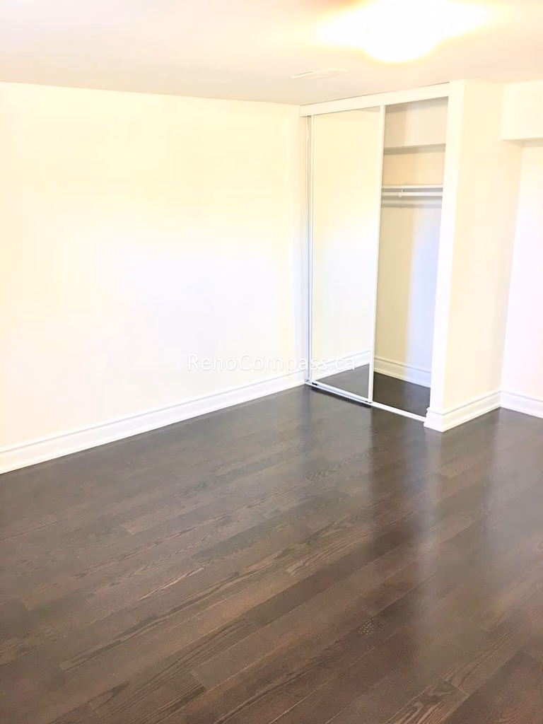 This Toronto basement renovation features a newly finished bedroom with rich hardwood flooring, fresh neutral walls, and a built-in closet with sliding doors. The clean layout and warm lighting create a comfortable and functional living space ideal for rental or family use. Completed by a professional Toronto renovation company, this basement bedroom upgrade enhances both property value and everyday living comfort.