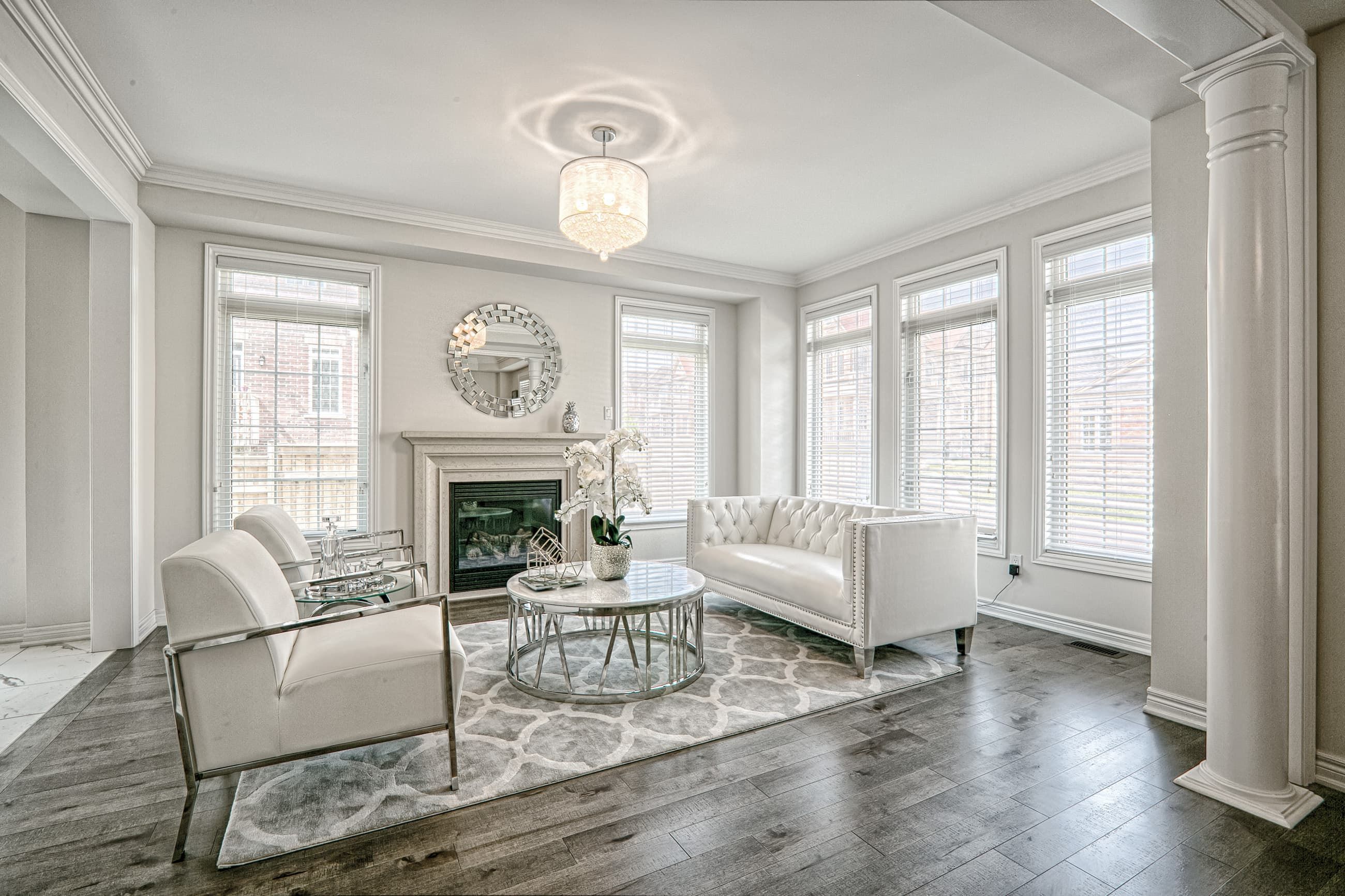 This Toronto luxury living room renovation features a modern classic interior with bright natural lighting, large windows, and elegant white finishes. The space showcases premium hardwood flooring, custom fireplace detailing, decorative columns, and sophisticated lighting fixtures that create a refined and welcoming atmosphere. Designed by a professional Toronto renovation company, this project blends timeless elegance with contemporary comfort, delivering a high-end residential interior perfect for modern family living.