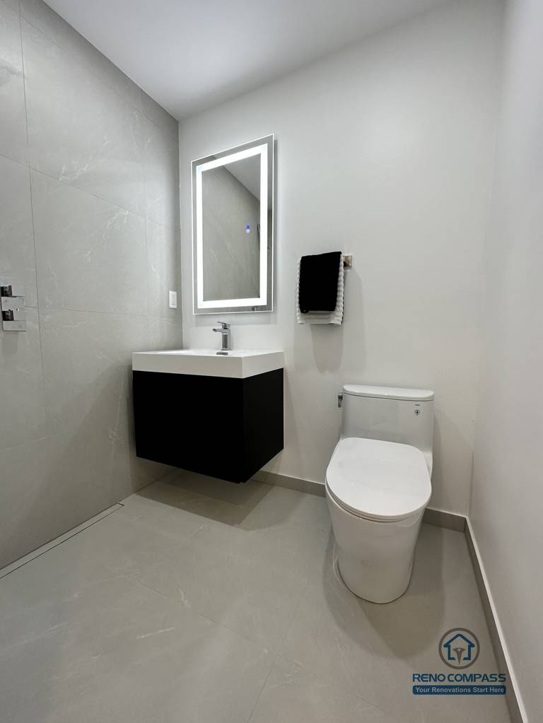 This image showcases a modern accessible pet shower bathroom renovation in Brampton, designed with a clean, barrier-free layout for ease of use. The space features large-format non-slip floor tiles, a wall-mounted floating vanity, an LED backlit mirror, and a compact toilet configuration to maximize maneuverability. The open shower area allows safe and comfortable bathing for pets while remaining fully accessible for homeowners. This type of thoughtful, functional design is ideal for aging-in-place and pet-friendly homes, completed by a professional Toronto Renovation Company with experience in accessibility-focused bathroom solutions.