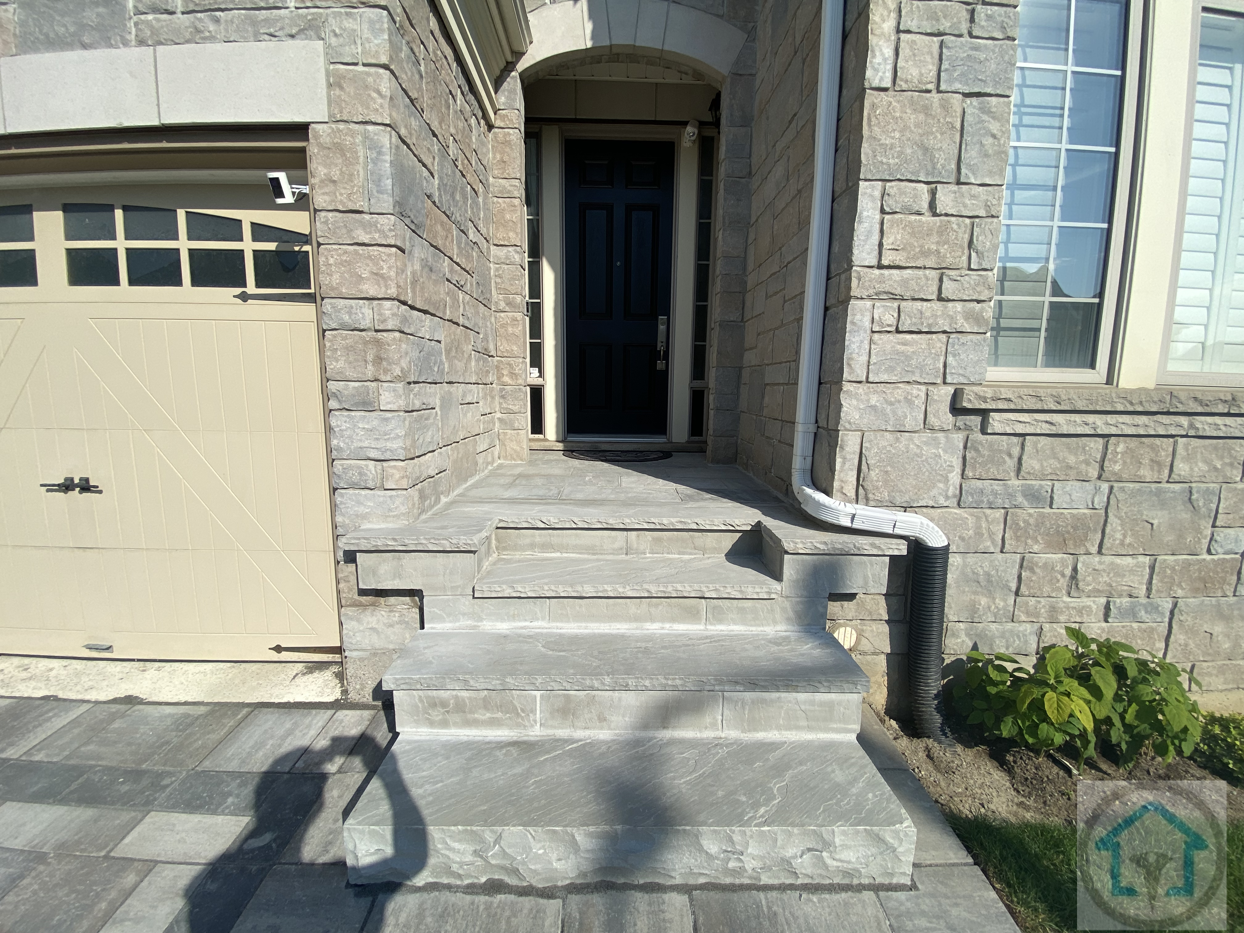 这张图片展示了位于 Richmond Hill 的住宅前门入口铺砖与台阶施工效果。入口区域采用统一色调的石材铺设，台阶比例合理，层次清晰，既满足日常上下通行的舒适度，也增强了整体立面的稳重感。铺砖与外墙石材、车库入口自然衔接，细节处理干净利落，同时兼顾防滑与耐用性，使前门空间在实用之余，呈现出整洁、有质感的入户第一印象。