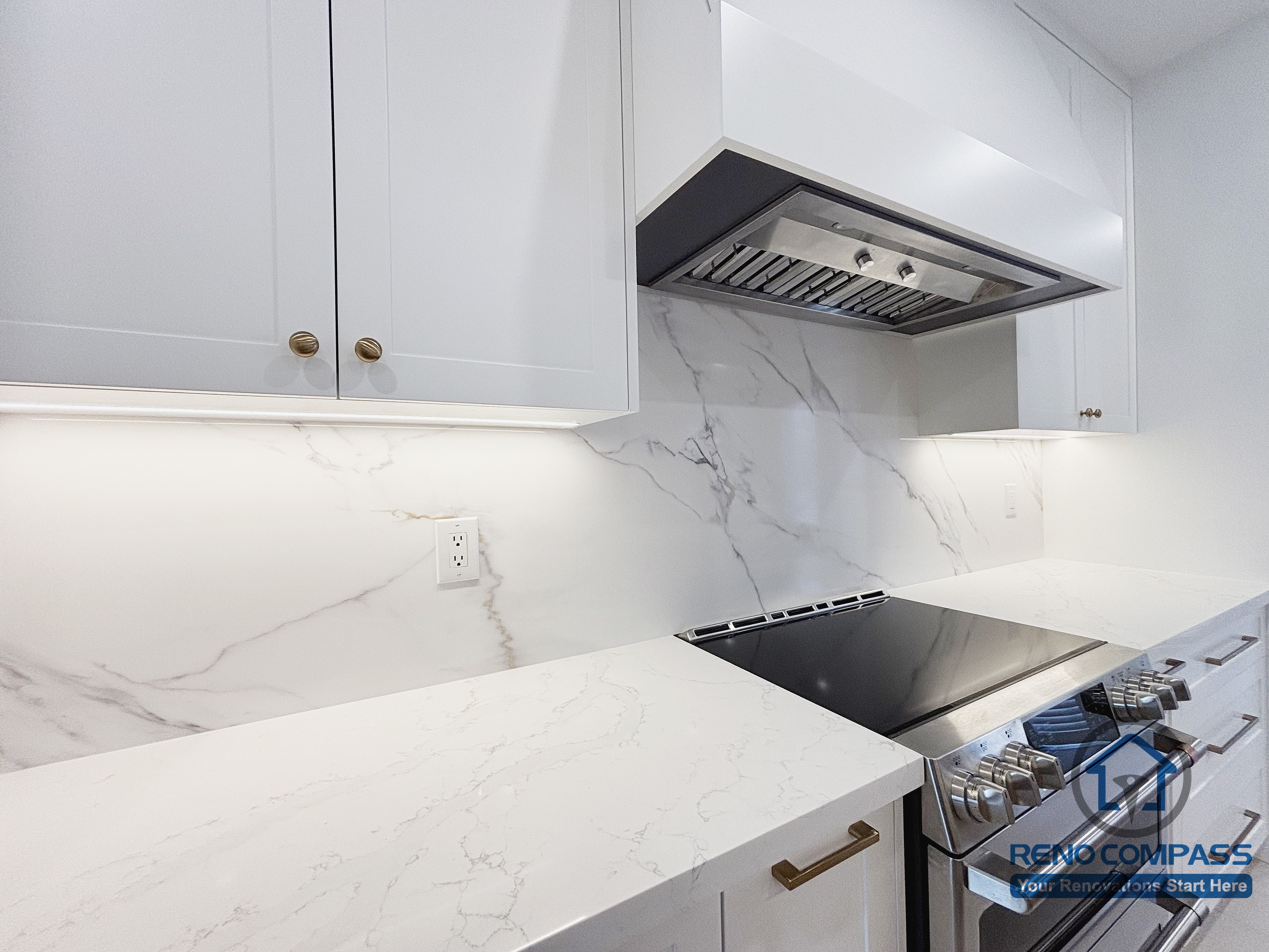 This Oakville kitchen renovation focuses on the main cooking detail, featuring a built-in range hood, quartz backsplash with subtle veining, and a clean, uninterrupted countertop surface. Precise alignment between cabinetry, hood, and appliances creates a refined and durable cooking zone designed for frequent use. Under-cabinet lighting enhances visibility while maintaining a calm visual tone. Completed by Reno Compass, this kitchen detail reflects careful craftsmanship and a long-term approach to modern Oakville kitchen renovation.