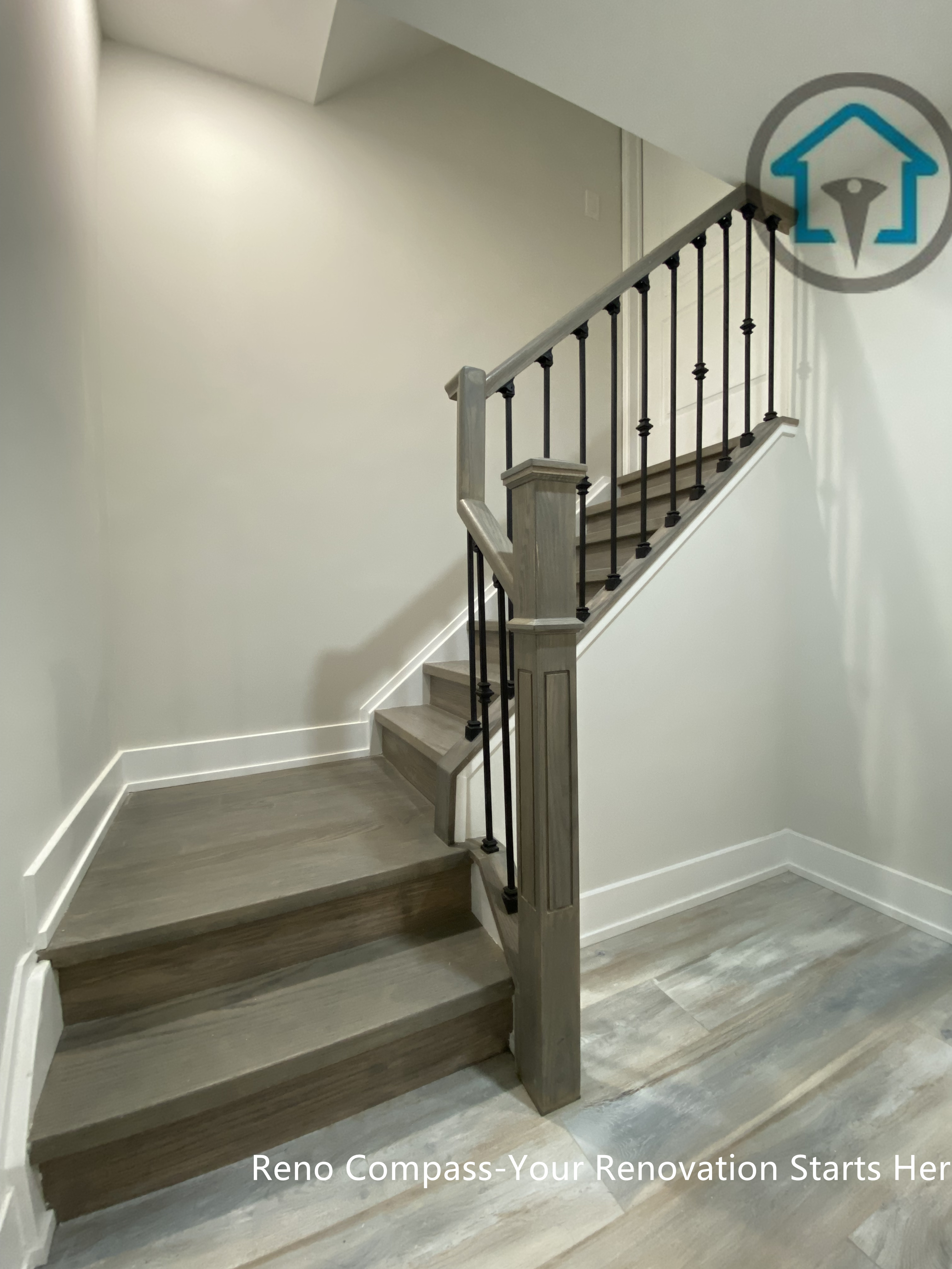This Stouffville basement renovation features a newly finished staircase with wood steps, matching flooring, and black metal railing. The updated stair design improves safety, durability, and visual continuity between basement levels, creating a clean and modern transition space completed by Reno Compass Inc.