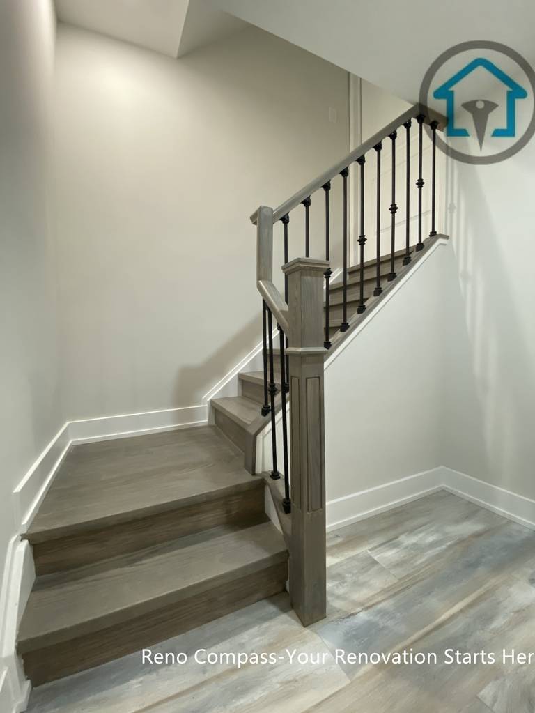 This Stouffville basement renovation features a newly finished staircase with wood steps, matching flooring, and black metal railing. The updated stair design improves safety, durability, and visual continuity between basement levels, creating a clean and modern transition space completed by Reno Compass Inc.