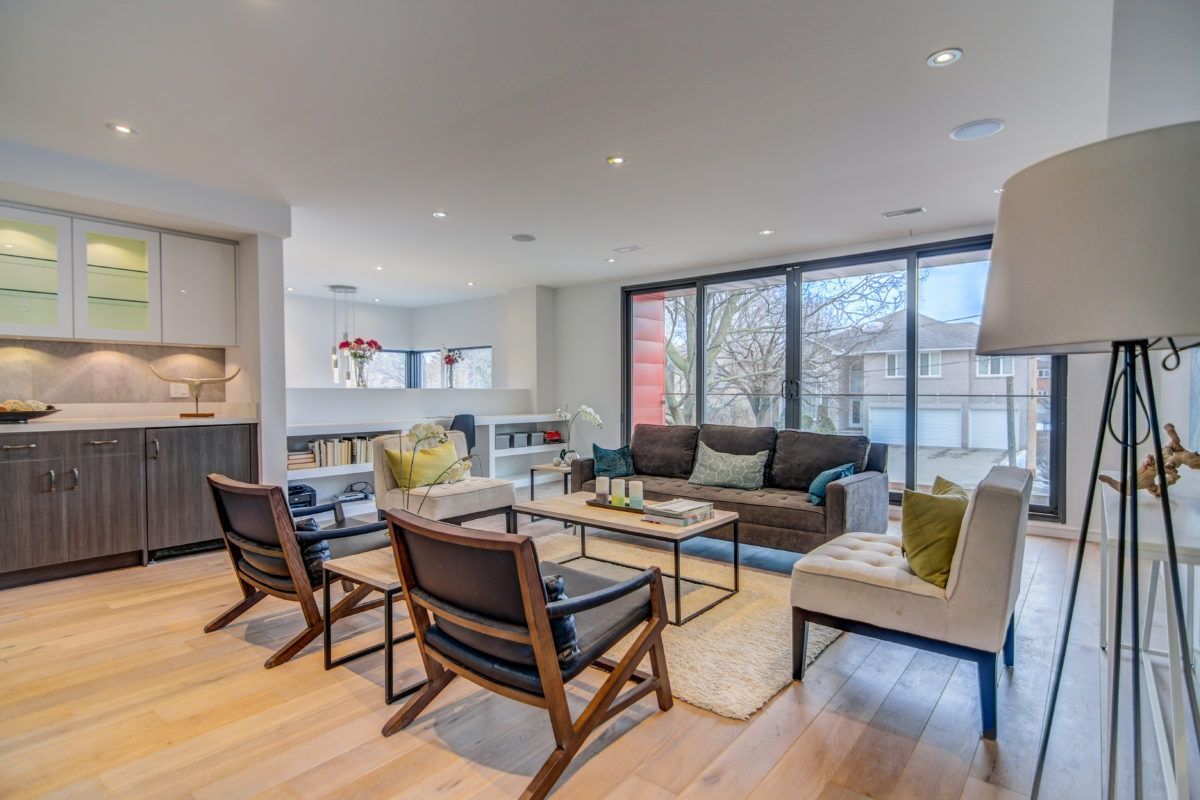 Contemporary open-concept living room renovation in Toronto featuring large floor-to-ceiling windows, light wood flooring, built-in cabinetry, and modern furniture layout. The bright and spacious design connects the lounge area with a custom bar and storage space, creating a comfortable and functional family living environment. Completed by a professional Toronto renovation company, this interior showcases modern luxury and everyday comfort.