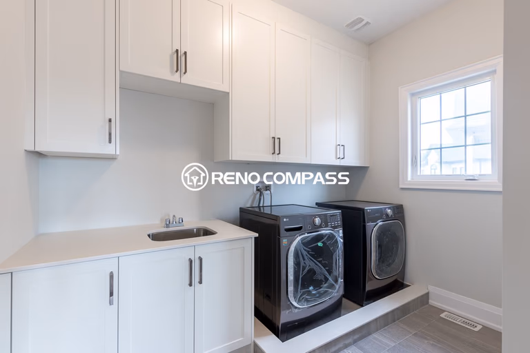 Functional laundry room renovation in Newmarket featuring custom white cabinetry, built-in sink, and raised washer and dryer platform. Completed by a professional Toronto renovation company, this design maximizes storage and creates a clean, organized laundry space.