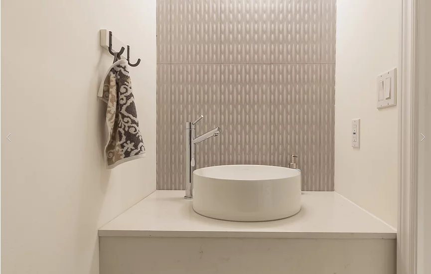 A sleek powder room from our Vaughan full house renovation featuring a floating vanity with vessel sink, custom faucet fixtures, and a textured accent wall tile. The minimalist design combines functionality and modern elegance in a compact, stylish space.