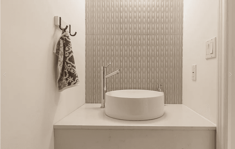 A sleek powder room from our Vaughan full house renovation featuring a floating vanity with vessel sink, custom faucet fixtures, and a textured accent wall tile. The minimalist design combines functionality and modern elegance in a compact, stylish space.