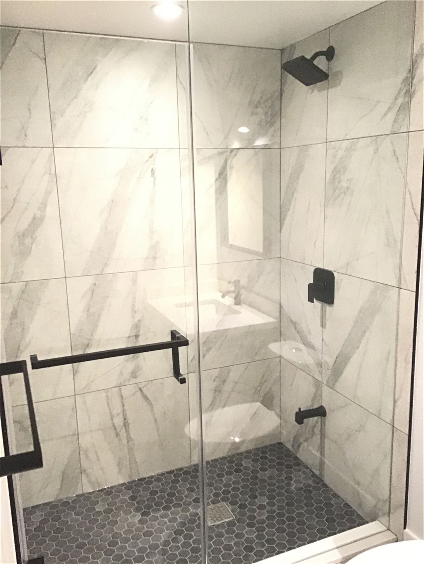 This Markham full home renovation showcases a modern shower design featuring large-format marble-look wall tiles, a sleek glass enclosure, and stylish hexagon floor tiles. Matte black fixtures and a built-in bench enhance both comfort and functionality. Completed by a trusted Toronto Renovation Company, this bathroom highlights premium materials and contemporary design.