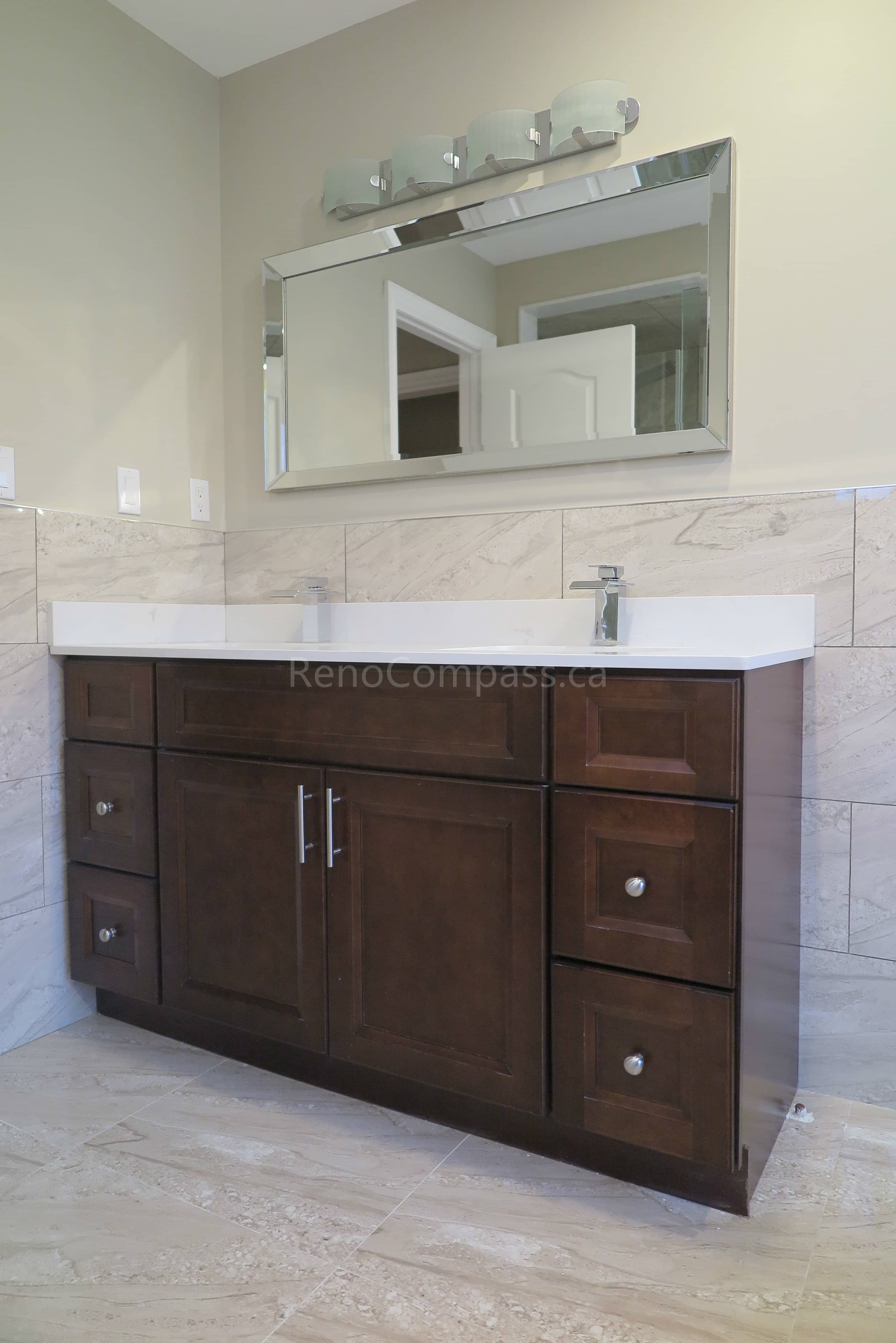 This Markham bathroom renovation features a custom dark wood vanity with a sleek quartz countertop and integrated sink, creating a clean and functional layout. Marble-style wall and floor tiles enhance the elegant and modern design, while updated lighting and mirror installation complete the refined look. Completed by Reno Compass, a professional renovation contractor specializing in bathroom renovations, vanity installation, and full interior remodeling across Markham and the Greater Toronto Area.