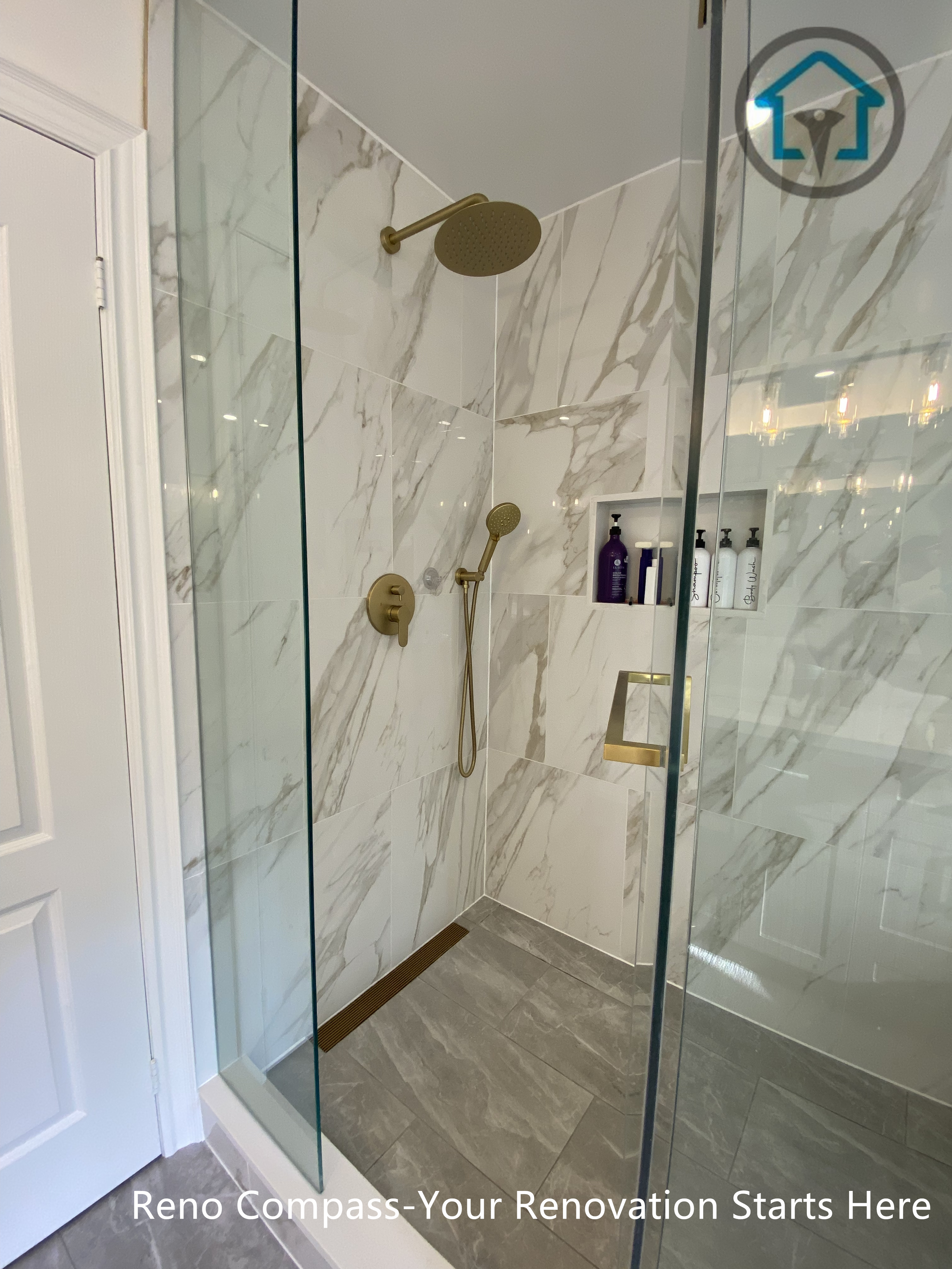 Frameless glass walk-in shower with marble-look wall tiles, built-in niche storage, and warm brass fixtures in a modern Markham bathroom.
