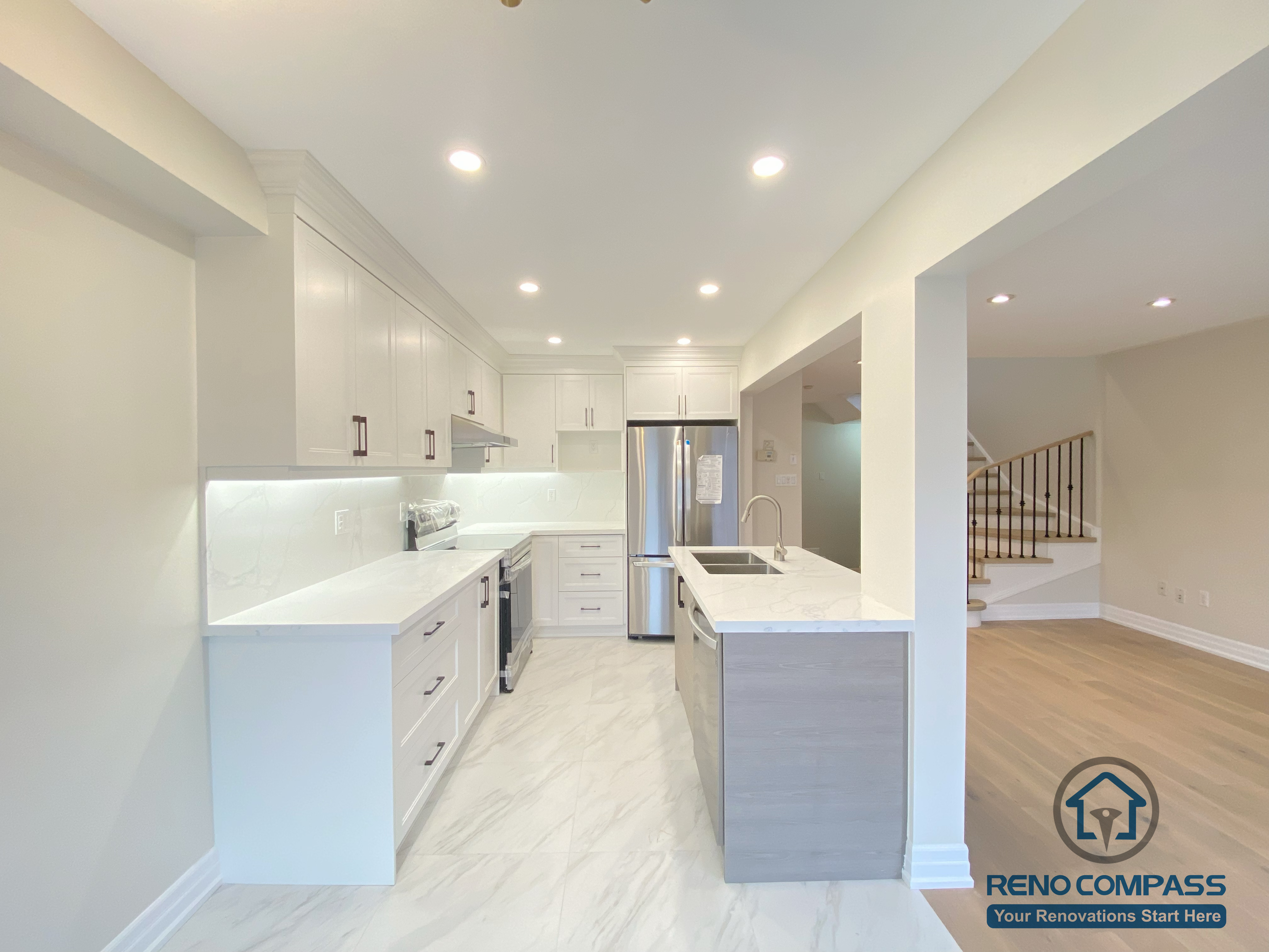This Markham interior renovation showcases a seamless open-concept layout connecting a modern kitchen with the adjacent living space. The design features custom white cabinetry, quartz countertops, a functional kitchen island, and integrated recessed lighting. Warm hardwood flooring enhances the living area, while the clean lines and neutral palette create a bright, spacious feel. Completed by a trusted Toronto renovation company, this project balances modern design, comfort, and everyday practicality for Markham homeowners.