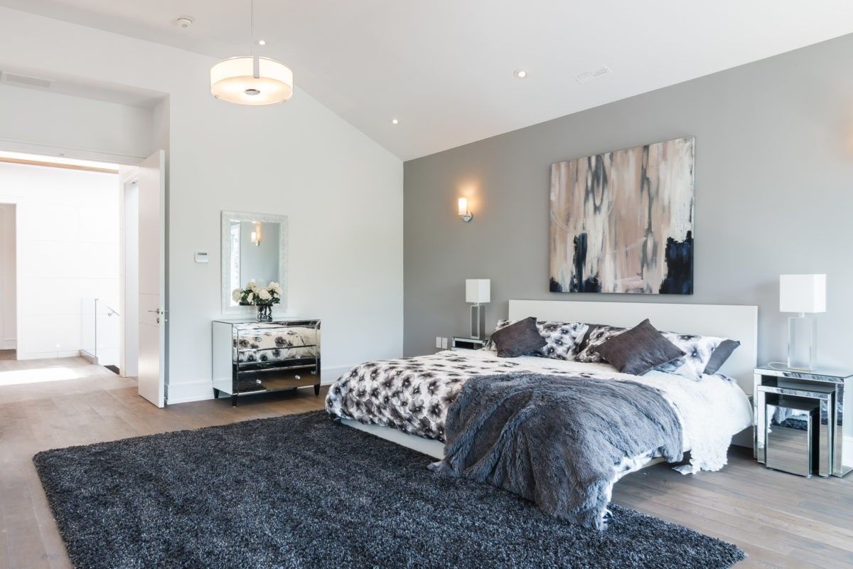 This Toronto modern interior renovation showcases a spacious master bedroom designed with soft neutral tones, plush textures, and elegant lighting fixtures. The room features wide-plank flooring, minimalist furniture, and a balanced layout that creates a calm, comfortable, and luxurious retreat within the home.