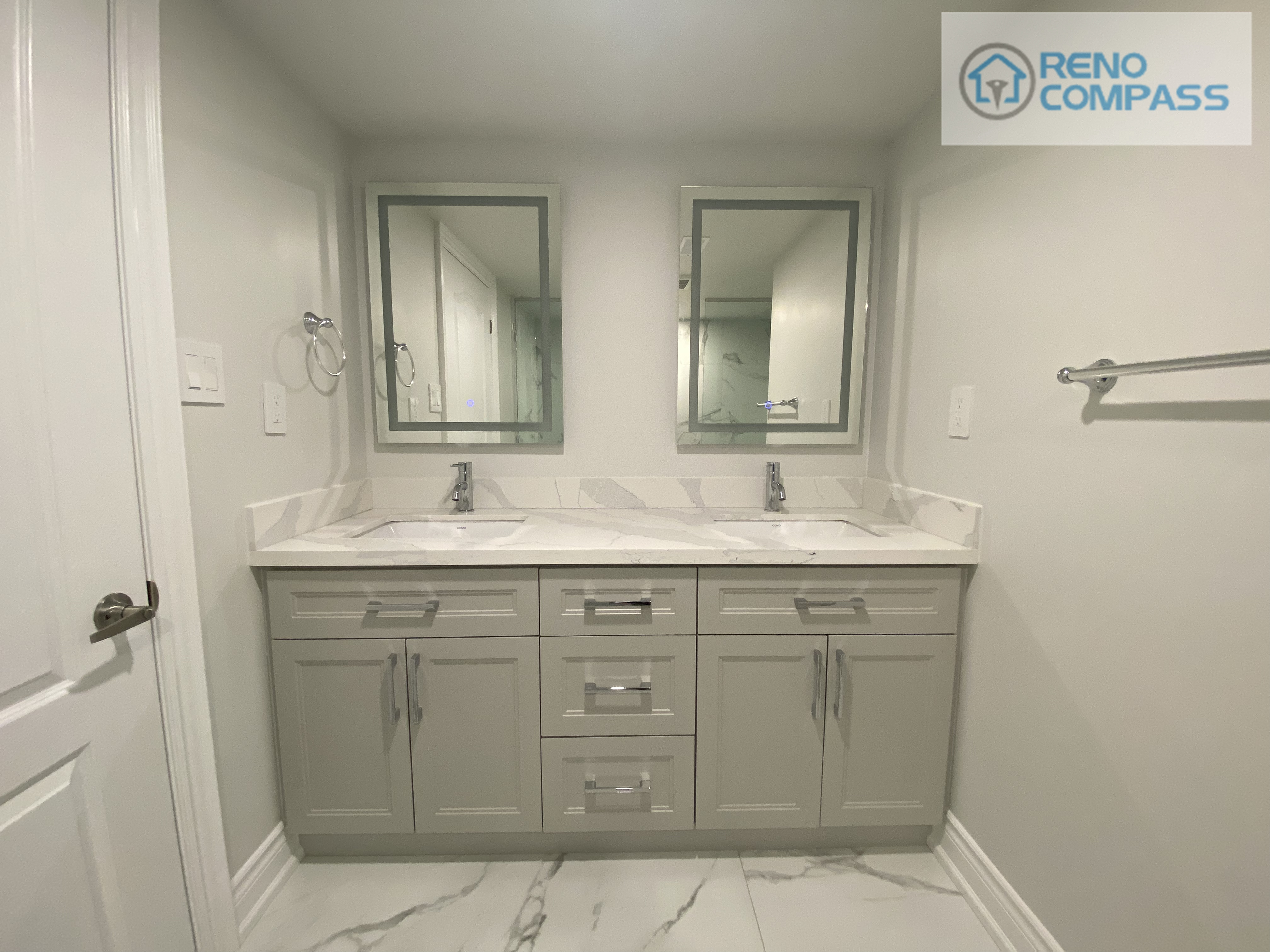This Woodbridge basement bathroom renovation features a clean and functional double vanity design, ideal for shared use and daily convenience. The custom cabinetry provides ample storage while maintaining a streamlined appearance. A quartz countertop with subtle veining enhances durability and brightness, paired with integrated sinks and modern chrome fixtures for a cohesive look. Framed mirrors and neutral wall tones help reflect light and visually expand the space, making the basement bathroom feel open and comfortable. Completed by Reno Compass, a Toronto renovation contractor specializing in basement and bathroom renovations.