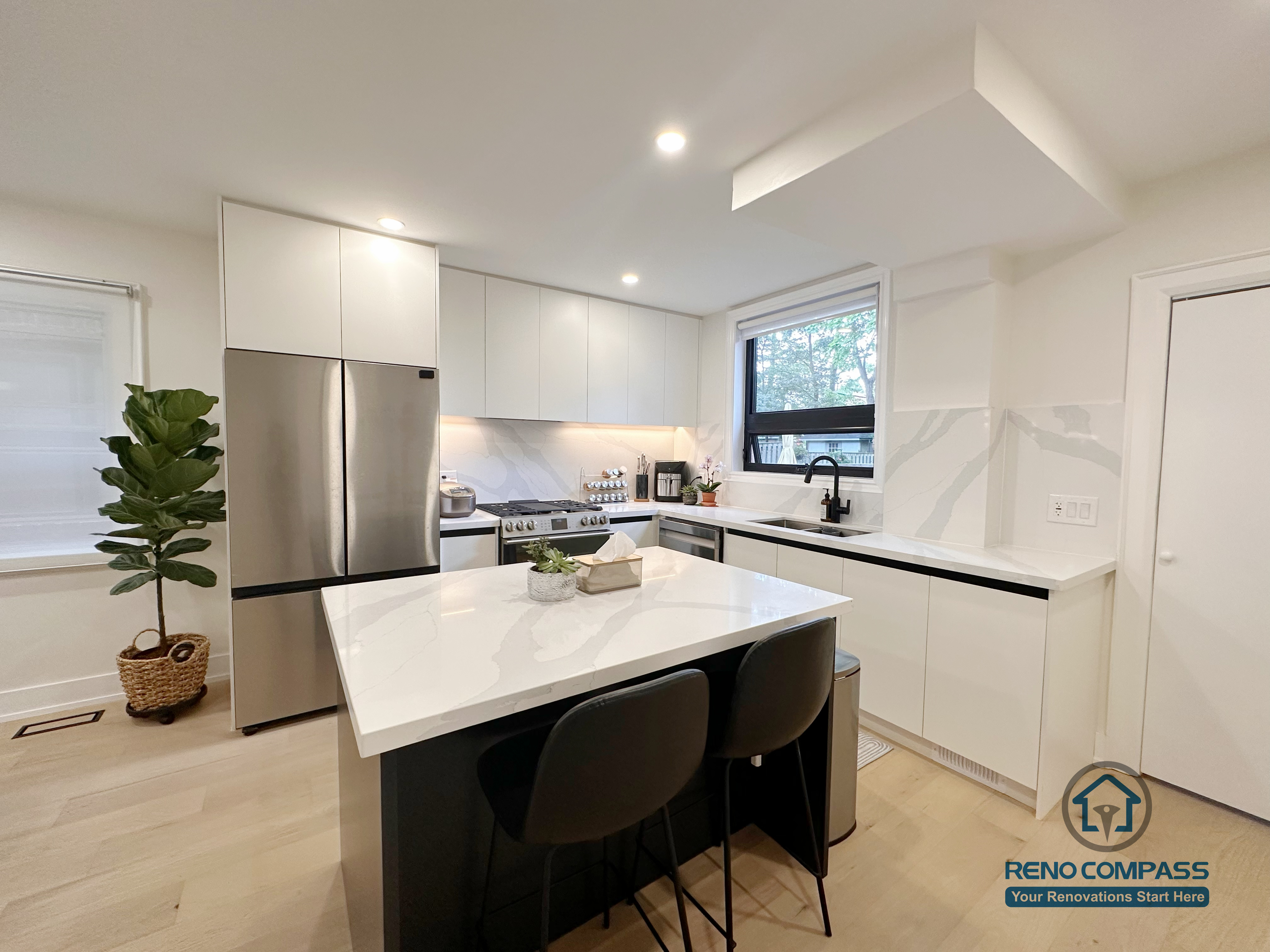 This Toronto interior renovation showcases a modern white kitchen featuring flat-panel cabinetry, a quartz waterfall island, stainless steel appliances, and recessed ceiling lighting. The clean lines and functional layout highlight contemporary kitchen design and quality workmanship delivered by a professional Toronto renovation company.