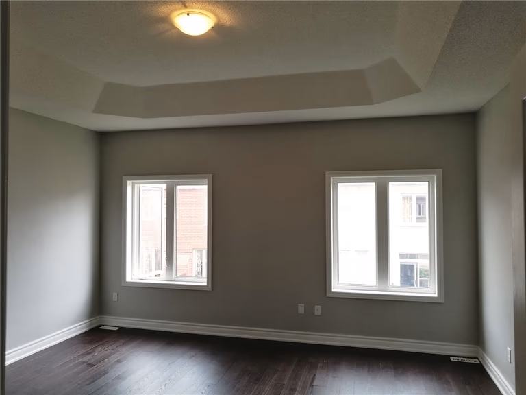 This image shows a bedroom after a Markham interior renovation, featuring a tray ceiling design, soft neutral wall colors, large windows for natural light, and dark hardwood flooring that creates a calm and balanced living environment.