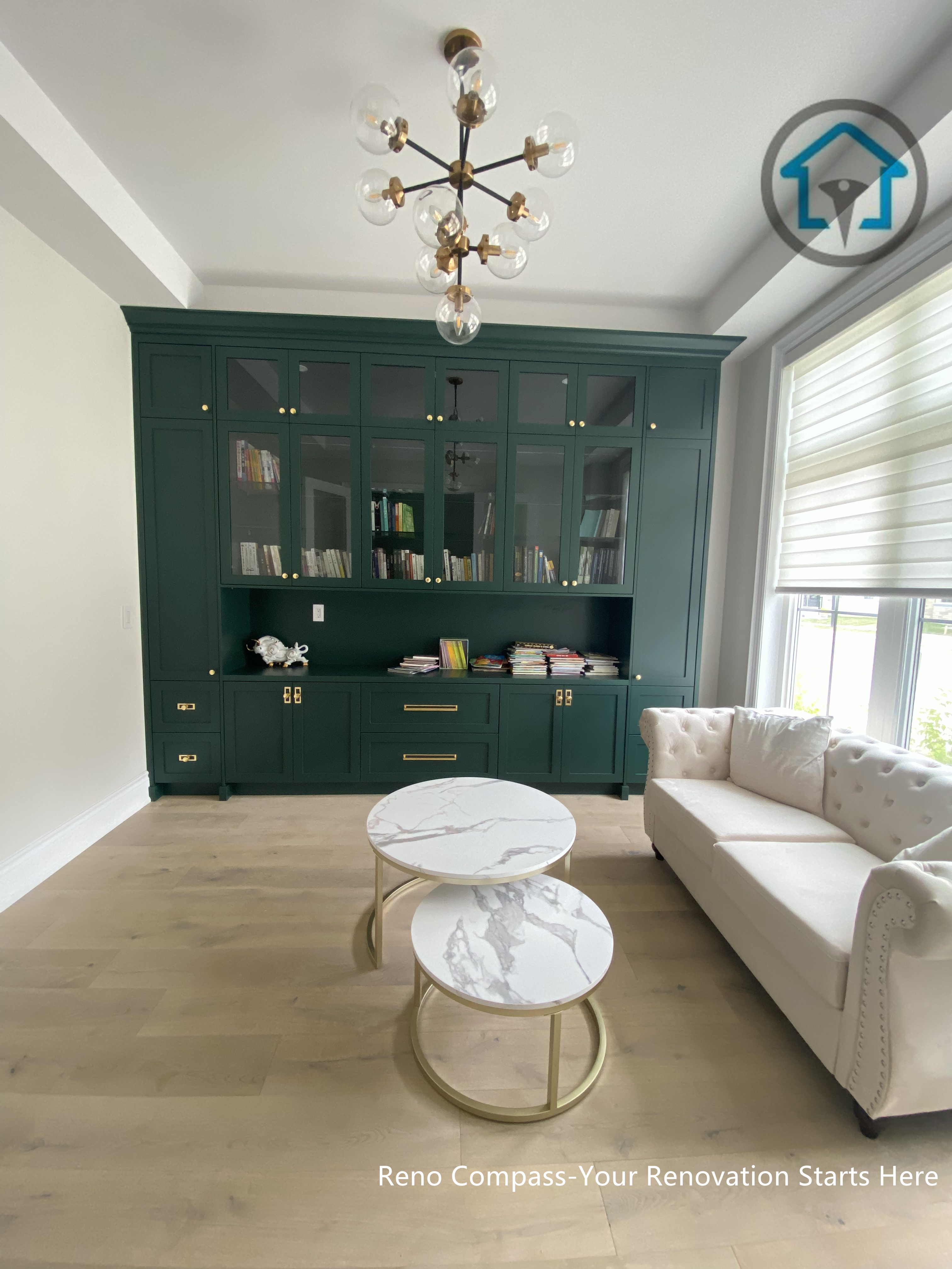 This image showcases a custom study and lounge renovation in Richmond Hill, featuring a full-height built-in cabinetry system in deep green tones with integrated shelving and storage. The space is styled as a refined reading and relaxation area, combining classic millwork details, warm wood flooring, and elegant lighting to create a calm yet sophisticated atmosphere. Designed and built by Reno Compass, this interior renovation highlights thoughtful custom cabinetry and balanced proportions tailored for everyday living.