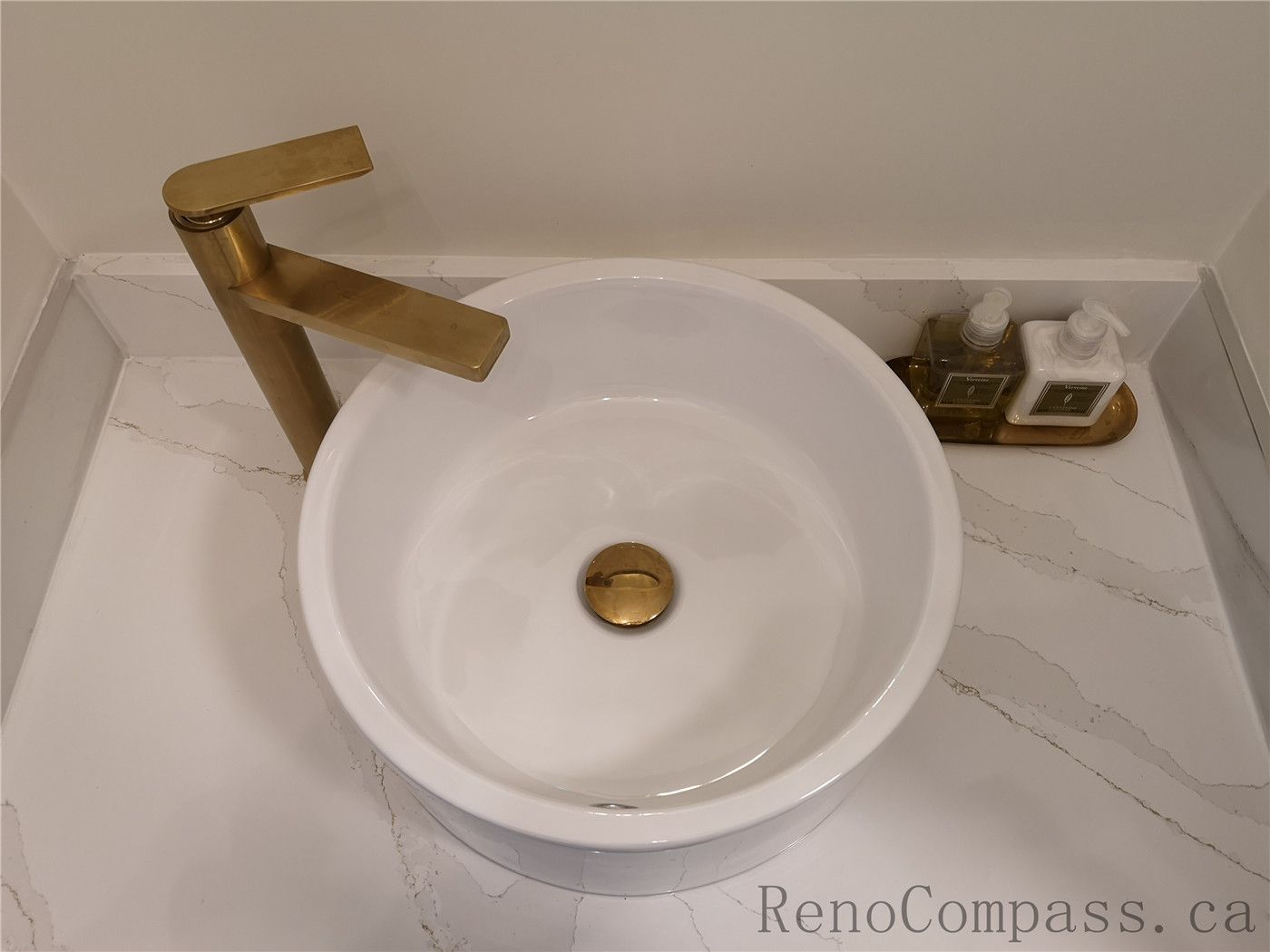 This Aurora bathroom renovation highlights a modern vanity design featuring a round vessel sink, quartz countertop, and elegant brushed gold faucet. The clean white surface paired with warm metallic fixtures creates a luxurious yet minimalist aesthetic. Completed by a professional Toronto renovation company with a focus on quality craftsmanship, functional layout, and contemporary interior finishing.