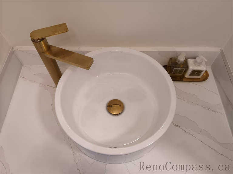 This Aurora bathroom renovation highlights a modern vanity design featuring a round vessel sink, quartz countertop, and elegant brushed gold faucet. The clean white surface paired with warm metallic fixtures creates a luxurious yet minimalist aesthetic. Completed by a professional Toronto renovation company with a focus on quality craftsmanship, functional layout, and contemporary interior finishing.