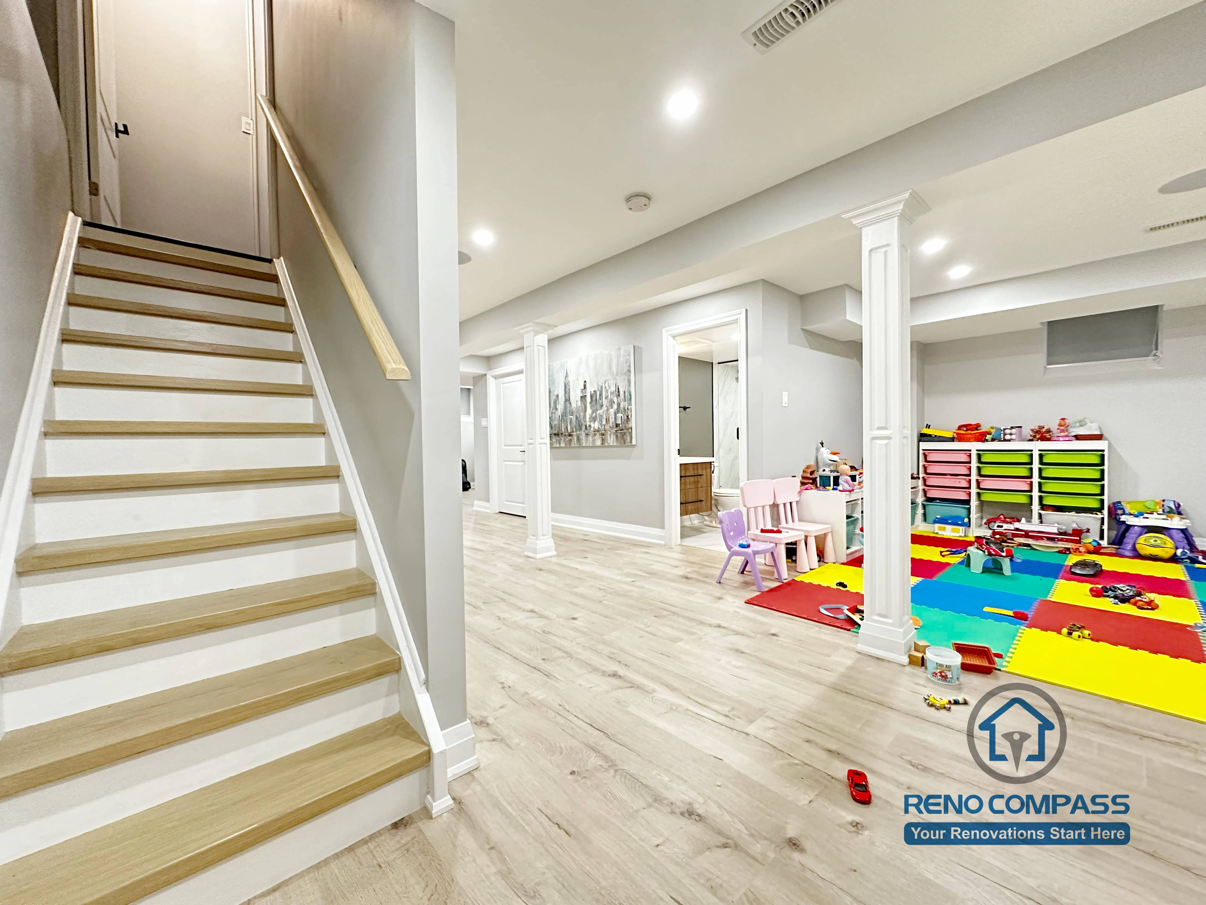 This Newmarket basement renovation showcases a bright open-concept layout with a custom staircase, modern column details, and durable wood-look flooring. The finished basement is designed for family use, featuring a spacious children’s play area, smooth ceiling finishes, and recessed lighting that enhances both functionality and comfort.
