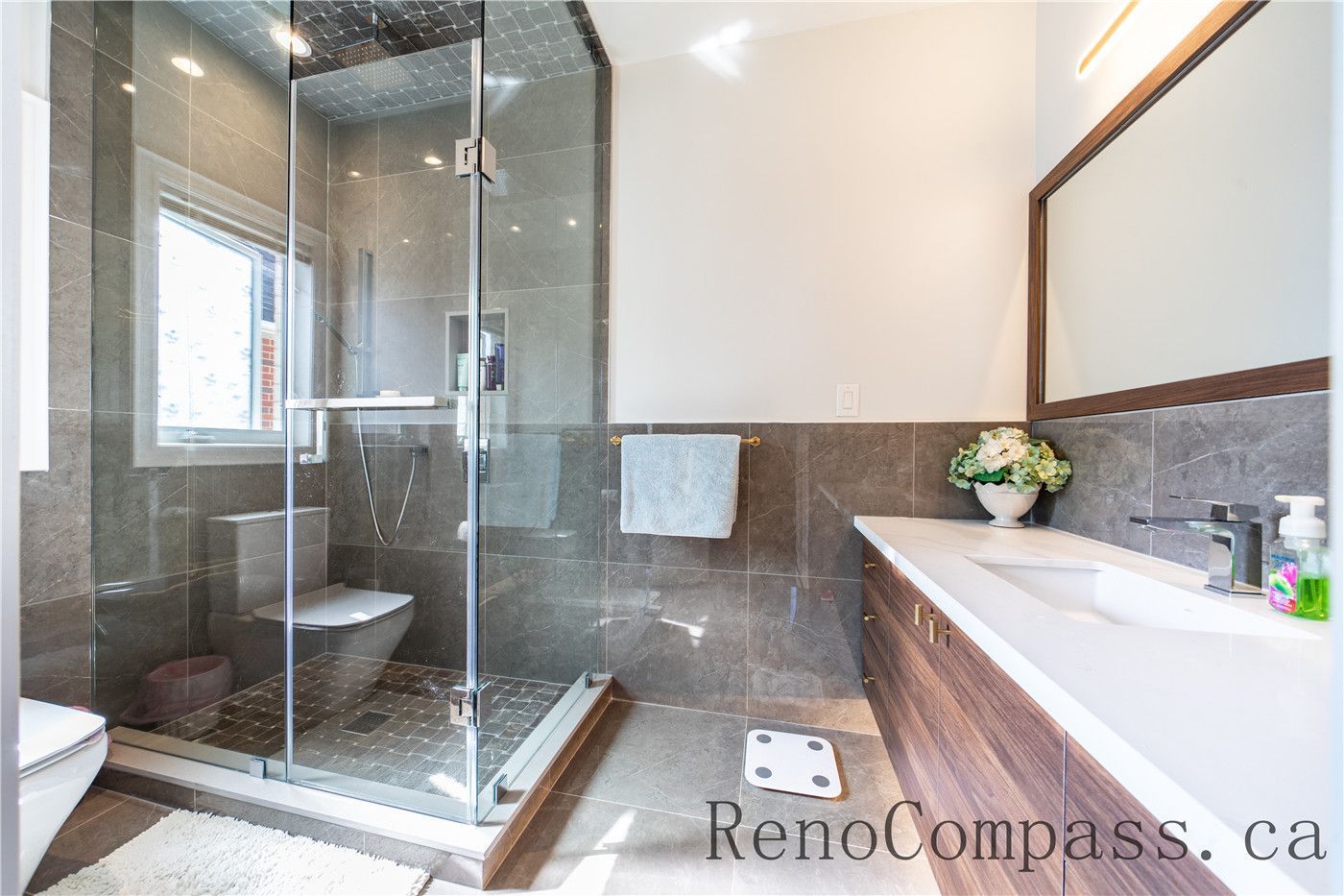 This Richmond Hill bathroom renovation features a custom wood vanity, quartz countertop, LED mirror lighting, and a frameless glass shower with modern fixtures. The clean layout and premium finishes create a spa-like atmosphere while enhancing functionality, showcasing the craftsmanship of a trusted Toronto renovation company specializing in complete home interior renovations.