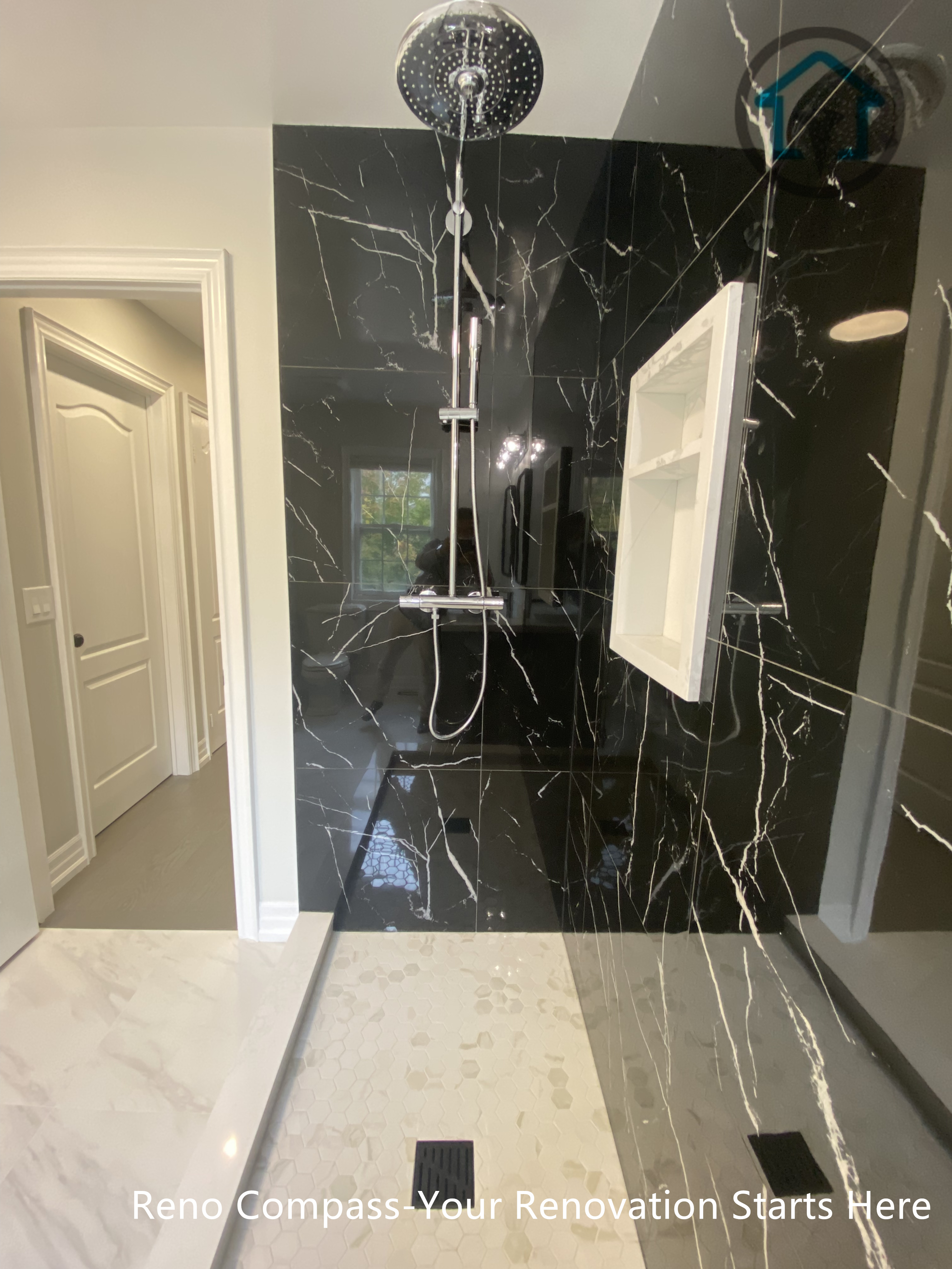 This shower design features a full-height black marble–look porcelain tile feature wall paired with a frameless glass enclosure. The rainfall shower system and clean tile alignment create a modern, hotel-inspired bathing experience, while the light-toned floor tile balances the dark wall for a refined and timeless finish.
