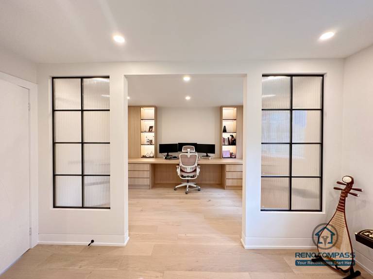 This Toronto home office renovation features light hardwood flooring, custom built-in desk cabinetry, and modern glass panel accents that create a bright and functional workspace. The open interior layout enhances natural light flow while maintaining visual separation, showcasing refined craftsmanship and flooring installation ideal for contemporary Toronto interior renovations.