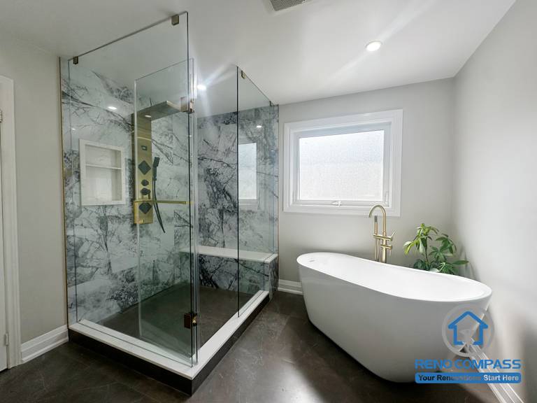 This Oakville bathroom renovation presents a well-balanced layout that places a frameless glass shower alongside a freestanding soaking tub. Marble-look wall surfaces, warm metal fixtures, and controlled natural light create a calm and cohesive atmosphere. The spatial arrangement emphasizes comfort, visual clarity, and efficient circulation, reflecting Reno Compass’s approach to practical, long-lasting bathroom design.