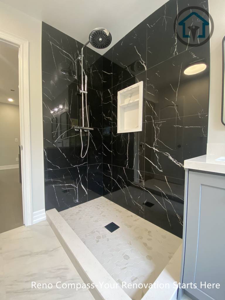 This walk-in shower showcases dramatic black marble–look porcelain tiles as a full-height feature wall. The rainfall shower system and integrated wall niche enhance both comfort and practicality, while the light shower base and floor tile create contrast and visual balance. The result is a bold yet refined shower design with a timeless, upscale feel.