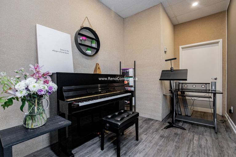 A cozy and professional private lesson room at The Singing School. This commercial interior features modern grey wood laminate flooring, custom textured wall finishes, and a glimpse into a feature room with industrial brick-style wallpaper. Expert commercial contracting in Richmond Hill.