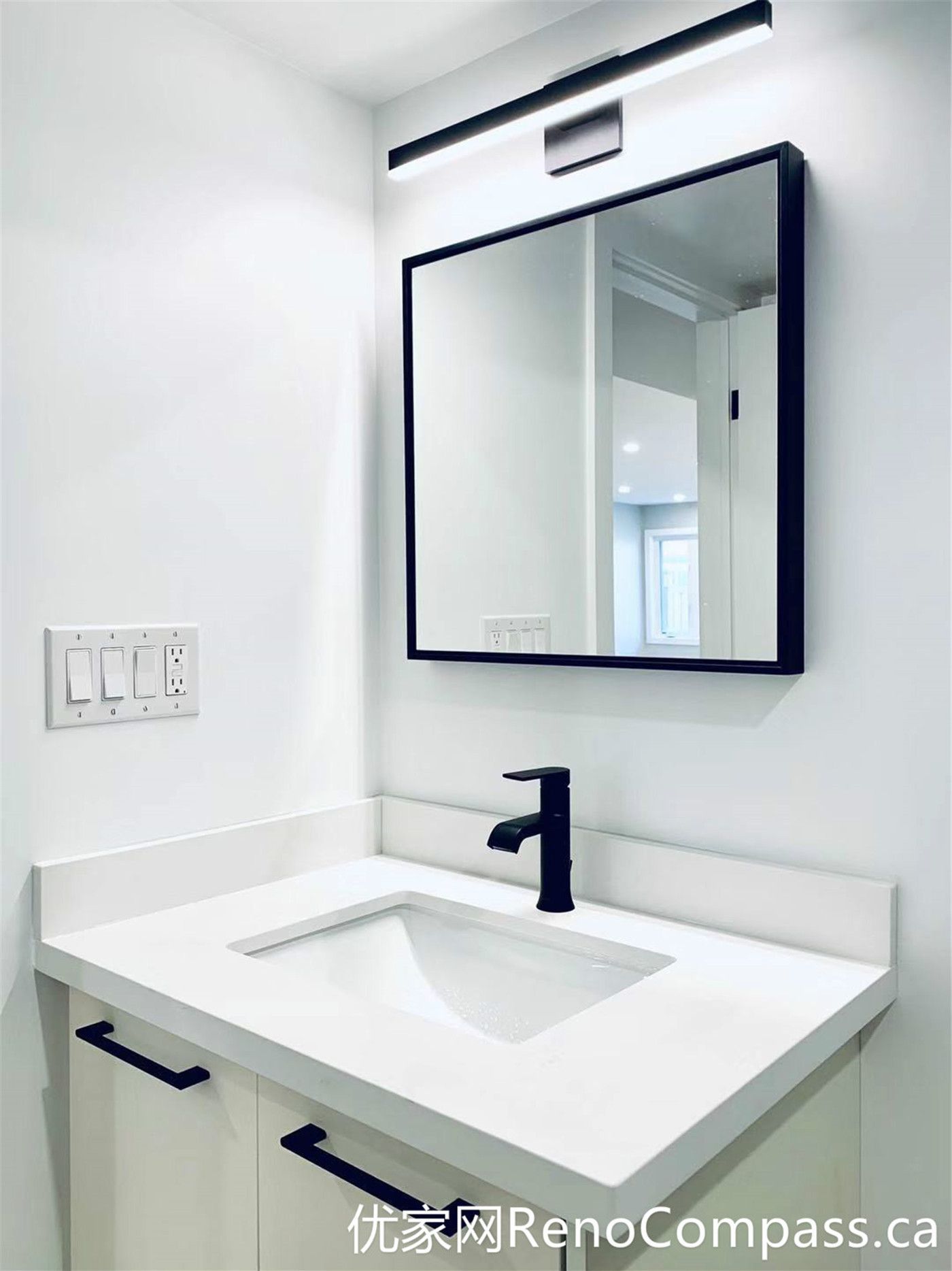 This bathroom from a Markham full home renovation showcases a sleek vanity design with an integrated sink, matte black faucet, and a clean-lined mirror with LED lighting. The minimalist white cabinetry paired with black accents creates a sharp, modern contrast while maintaining a bright and functional space.