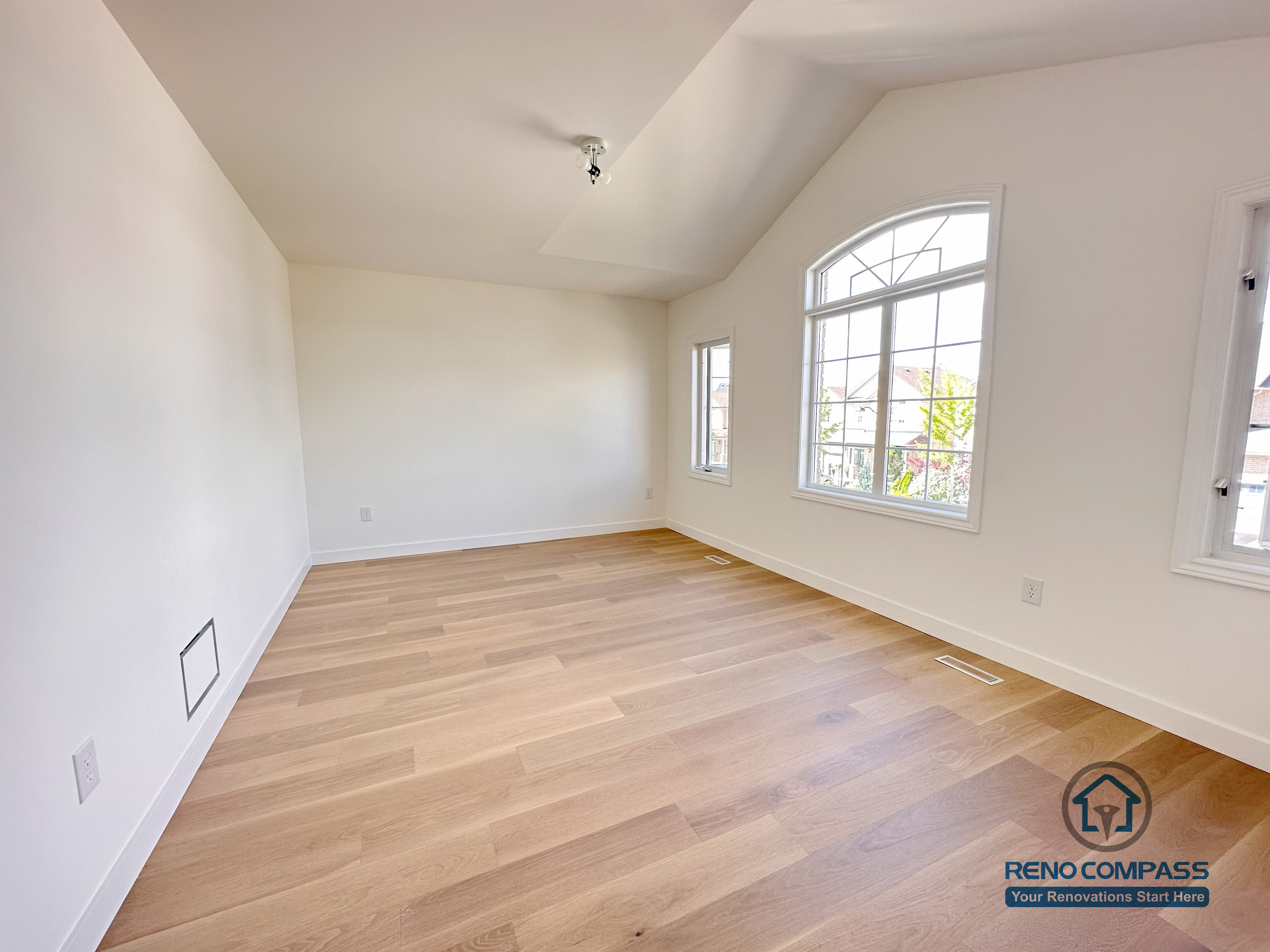 This image features a Markham bedroom flooring renovation with wide-plank hardwood floors, clean wall finishes, and abundant natural light from large arched windows. The simple layout emphasizes comfort, brightness, and everyday functionality, making the space suitable for a primary or secondary bedroom. Precise flooring installation ensures consistent plank alignment and long-term durability. Completed by a professional Toronto renovation company, Reno Compass Inc., this project reflects careful attention to residential flooring quality and livable interior design.