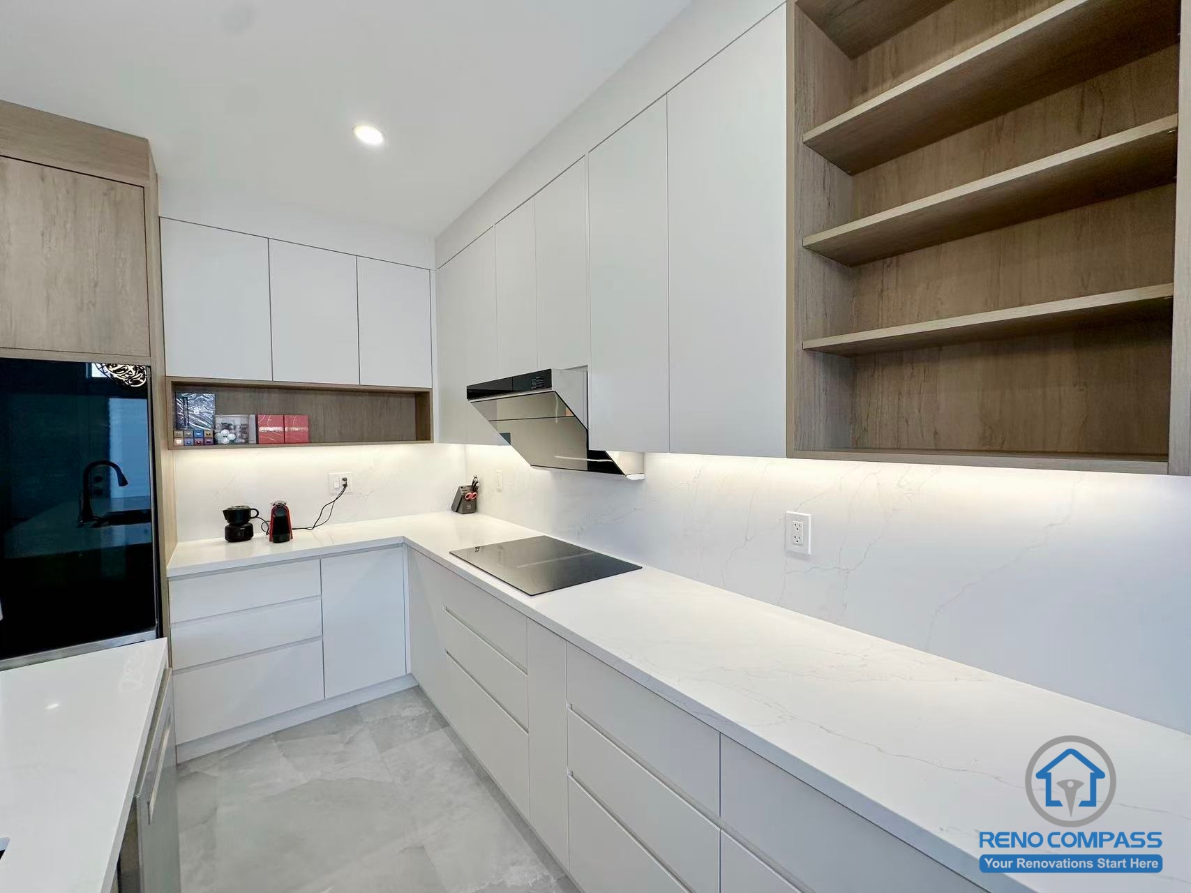 This Stouffville kitchen renovation showcases a clean, minimalist layout with flat-panel white cabinetry, warm wood open shelving, and full-height quartz countertops. Under-cabinet lighting enhances functionality and highlights the streamlined work area, creating a bright and modern cooking space. Completed by an experienced Toronto renovation company, Reno Compass Inc., this project reflects precise detailing and efficient kitchen planning.