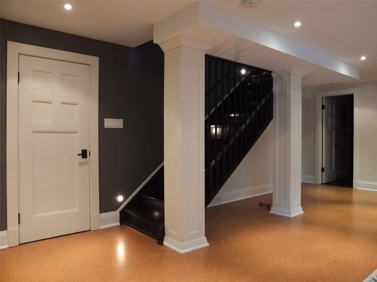 This Oakville basement renovation showcases a beautifully finished staircase area featuring decorative columns, modern recessed pot lights, and clean wall finishes. The warm cork flooring complements the dark staircase railing and accent wall, creating a stylish transition between basement levels. Completed by a professional Toronto Renovation Company, Reno Compass Inc., the project highlights detailed craftsmanship and thoughtful basement design.
