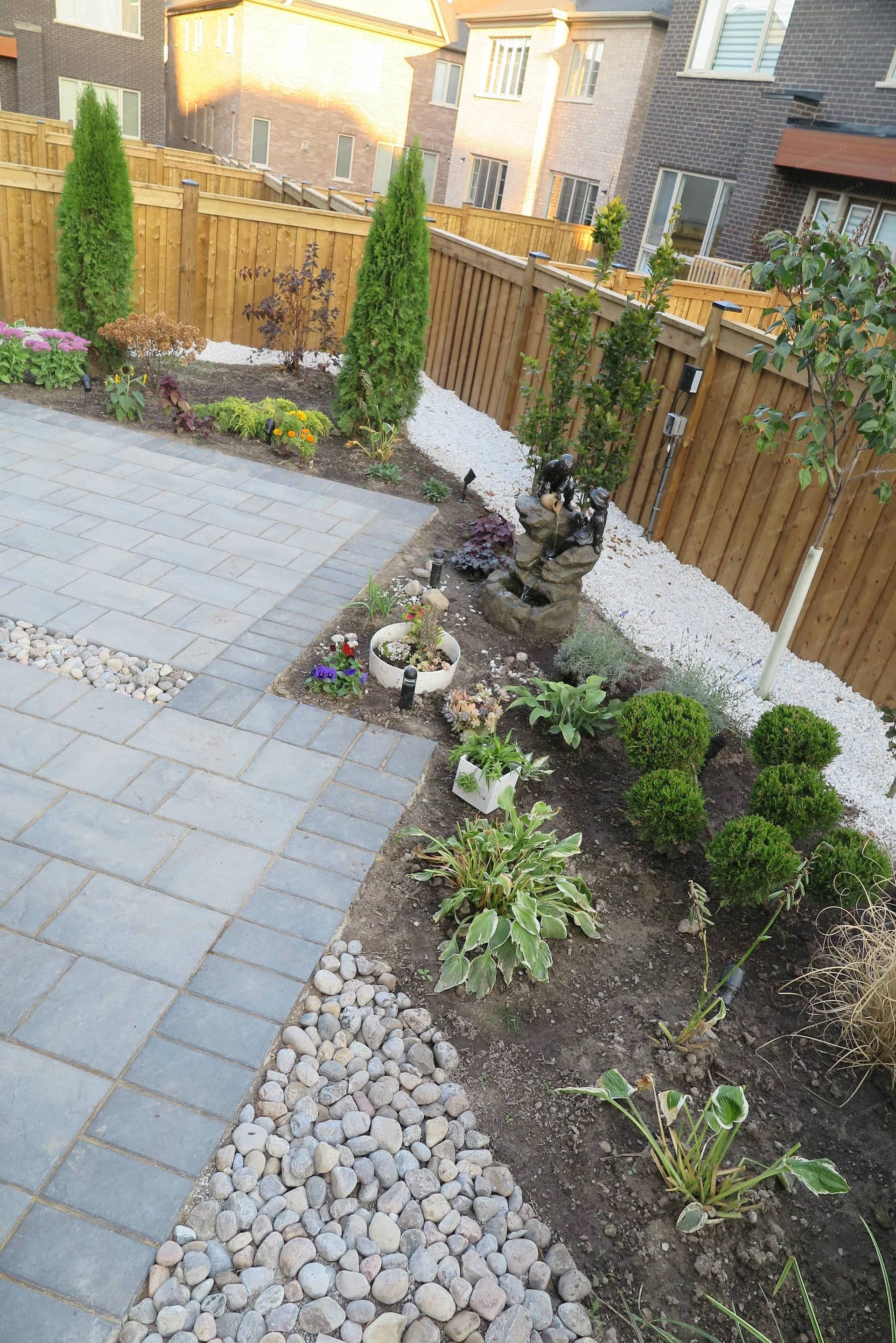 Backyard landscaping renovation in Vaughan featuring a modern interlocking patio, decorative river rock accents, layered garden beds, and a small ornamental water feature. This outdoor design blends hardscape and soft scape elements to create a relaxing backyard environment with strong visual balance and natural landscape texture.