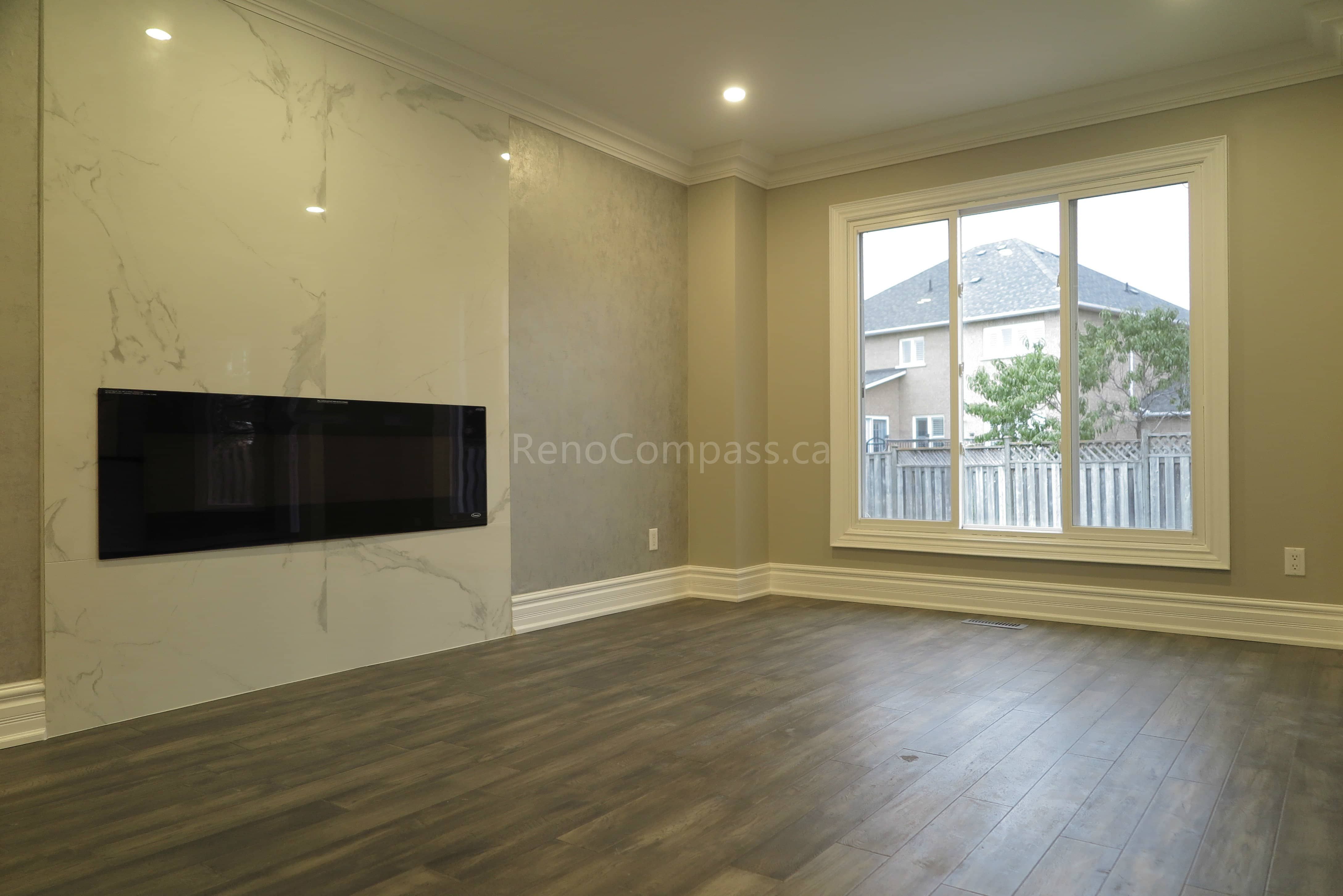 This Markham interior renovation highlights a modern living room upgrade featuring a sleek built-in linear fireplace and a marble-style feature wall. The space is finished with warm neutral paint tones, crown molding details, and newly installed dark hardwood flooring, creating a clean and elegant contemporary atmosphere. Completed by Reno Compass, a trusted renovation contractor providing professional interior renovation and custom finishing services in Markham and the Greater Toronto Area.